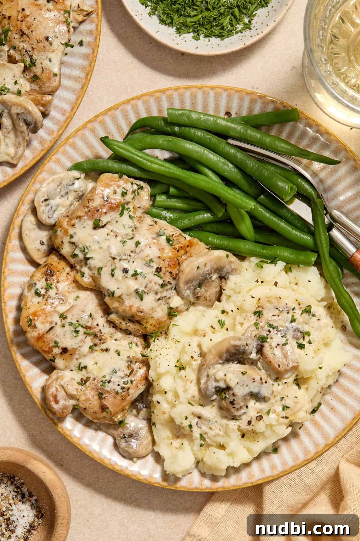 Creamy Mushroom Chicken Thighs with Garlic and Herbs 2 Cream plate with chicken thighs in creamy mushroom sauce and green beans and mashed potatoes.