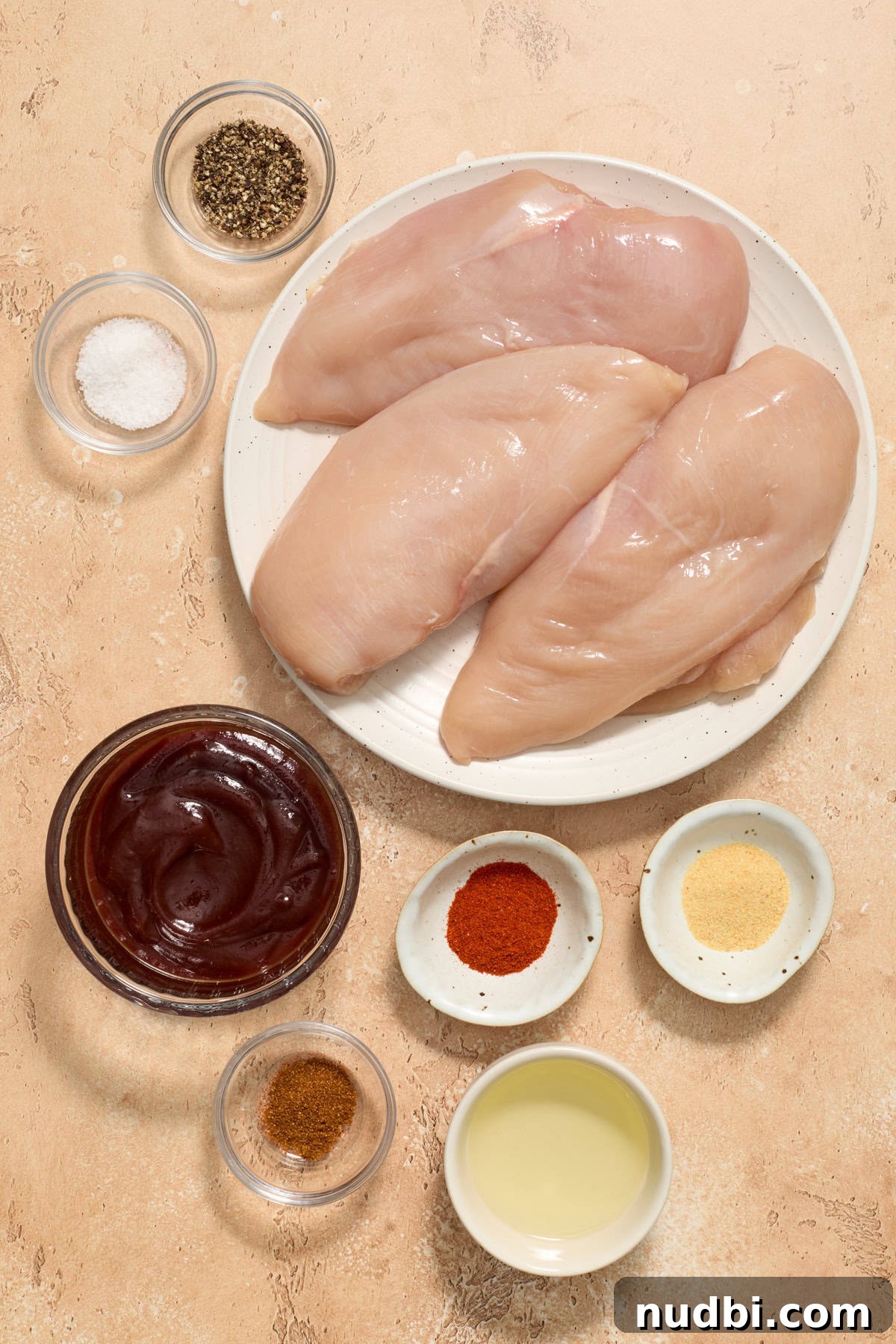 Juicy BBQ Chicken Breast in the Air Fryer — Quick Recipe 3 Raw chicken breasts, bbq sauce, seasoning and oil on surface.