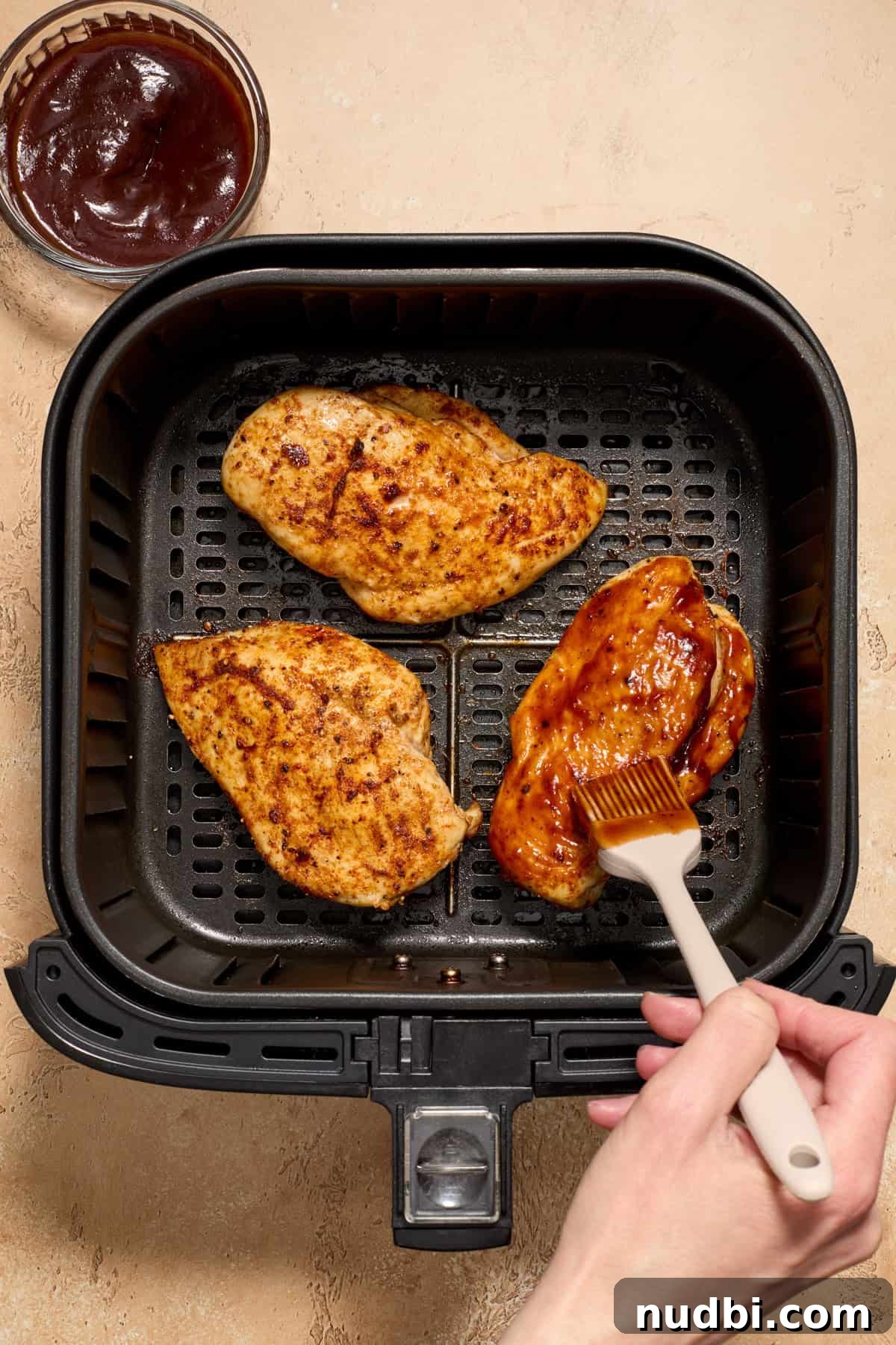 Juicy BBQ Chicken Breast in the Air Fryer — Quick Recipe 7 Air fryer basket with chicken with bbq sauce being brushed over top.