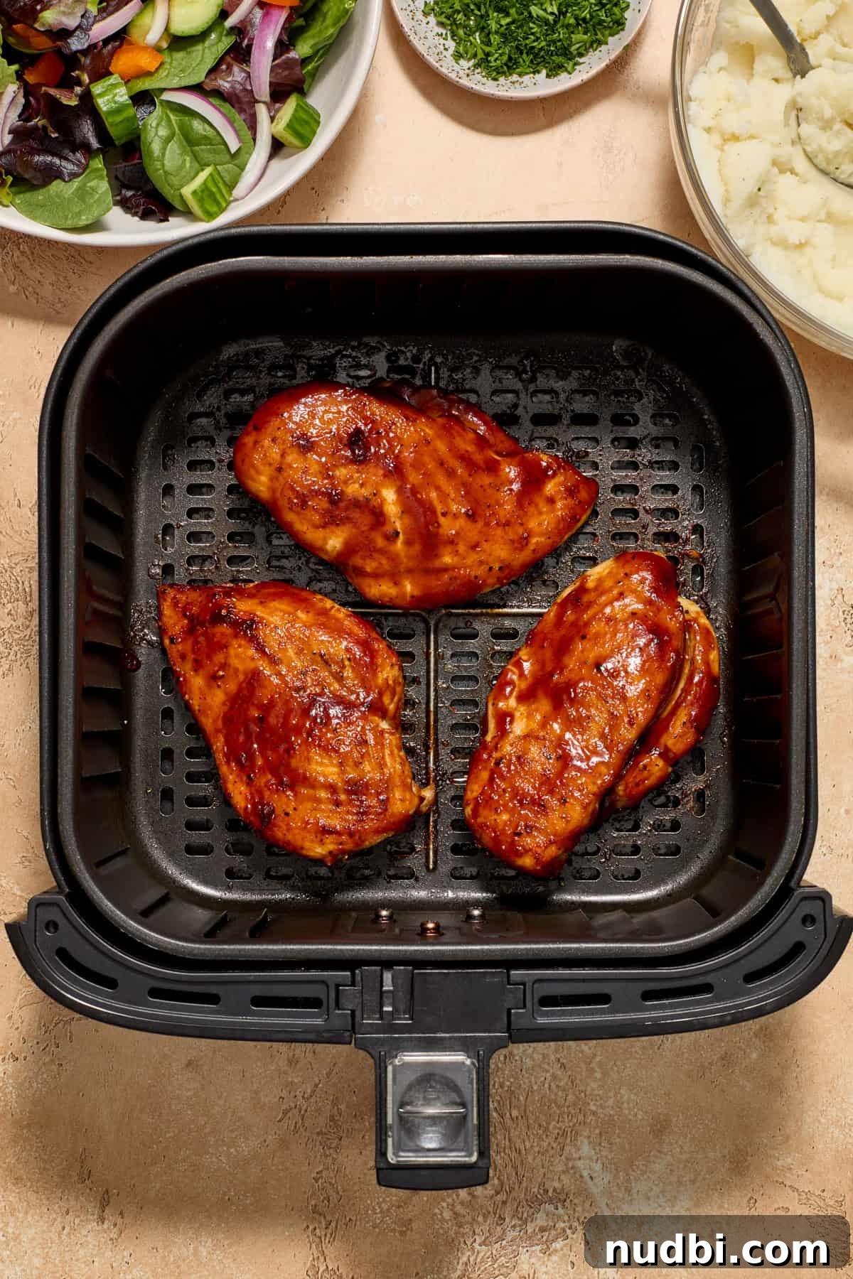 Juicy BBQ Chicken Breast in the Air Fryer — Quick Recipe 8 Cooked air fryer bbq chicken breast in air fryer basket with potatoes and salad in bowls beside the air fryer.