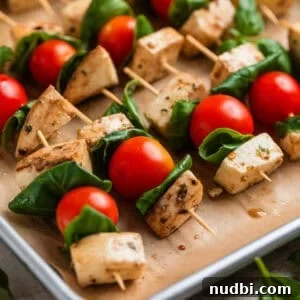 Marinated Mozzarella, Tomato & Basil Skewers for Entertaining 8 Tomato, basil mozzarella skewers lined up on parchment lined pan.