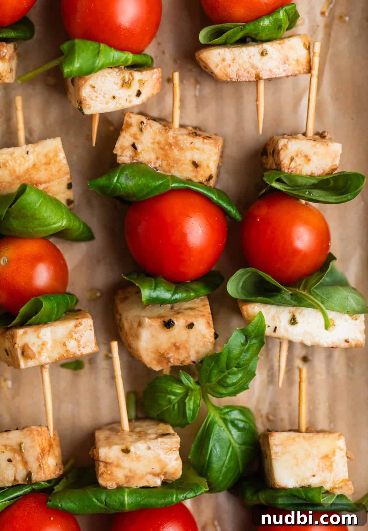Marinated Mozzarella, Tomato & Basil Skewers for Entertaining 3 Caprese salad skewers lined on parchment.