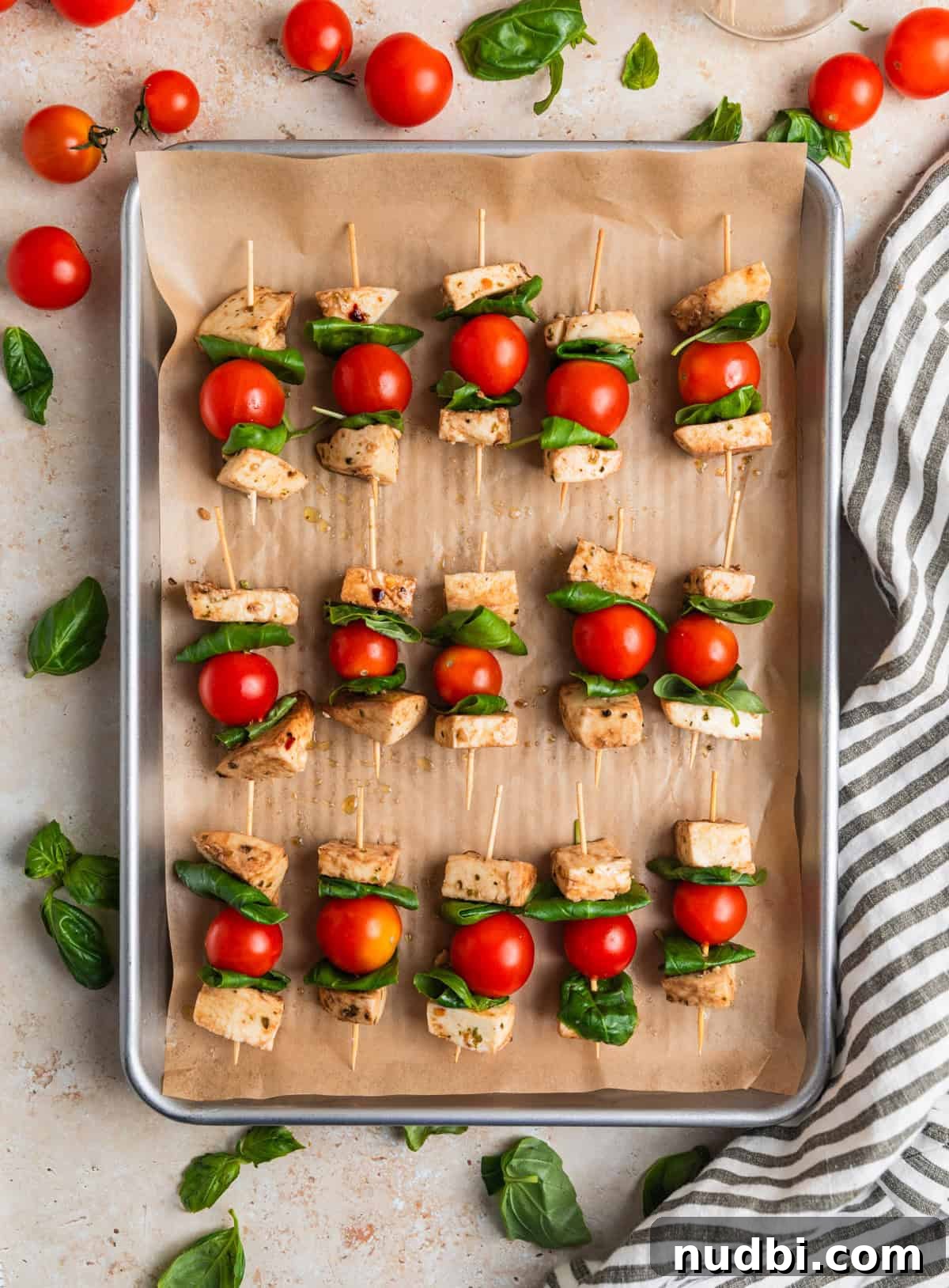 Marinated Mozzarella, Tomato & Basil Skewers for Entertaining 6 Skewers lined with grape tomatoes, basil leaves and marinated mozzarella on parchment lined cookie sheet.