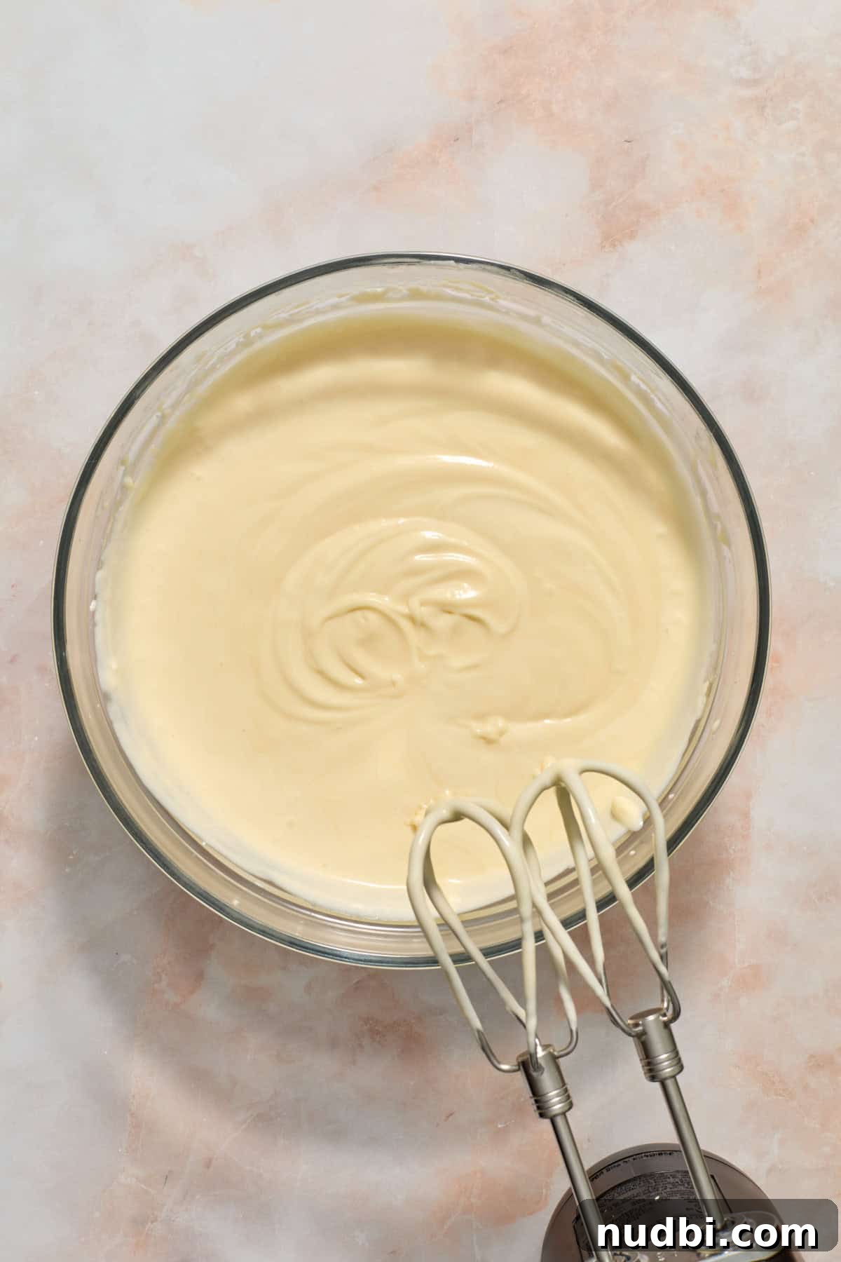 White Chocolate Raspberry Cheesecake Bars Recipe 13 White chocolate cheesecake mixture in glass mixing bowl with electric beaters offset.