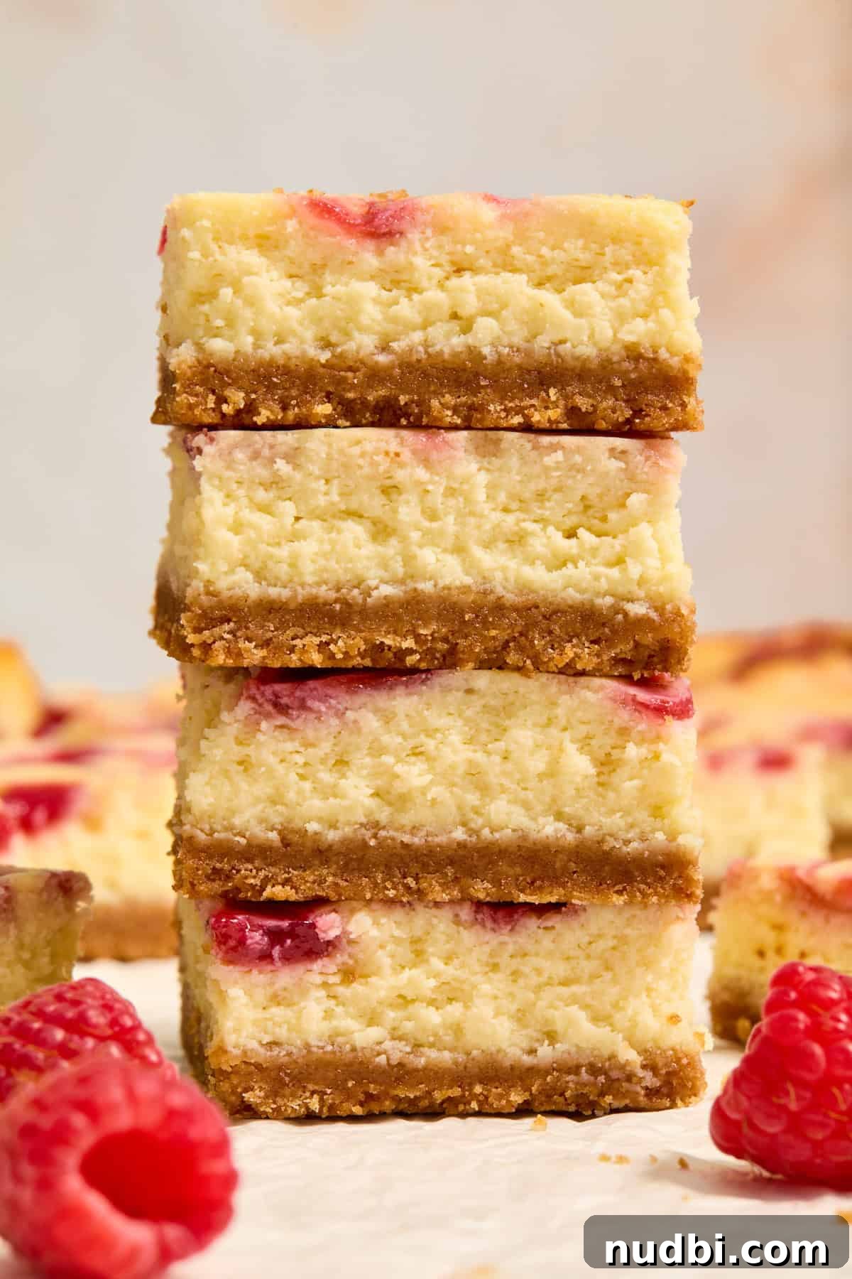 White Chocolate Raspberry Cheesecake Bars Recipe 14 Stacked raspberry white chocolate cheesecake bars with raspberries surrounding.