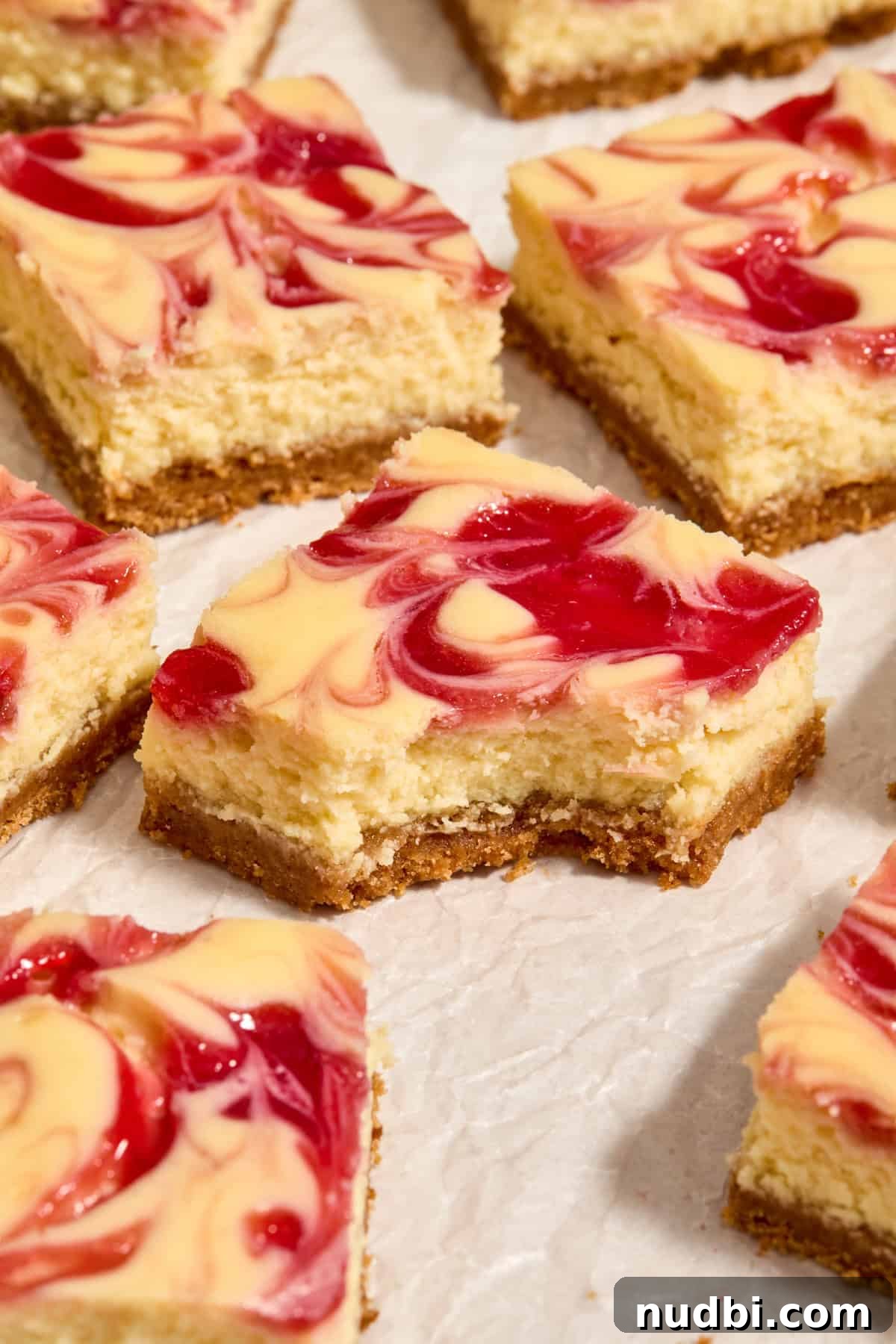 White Chocolate Raspberry Cheesecake Bars Recipe 3 Cheesecake bar square with bite taken out and arranged on wax paper with other cheesecake bar pieces.