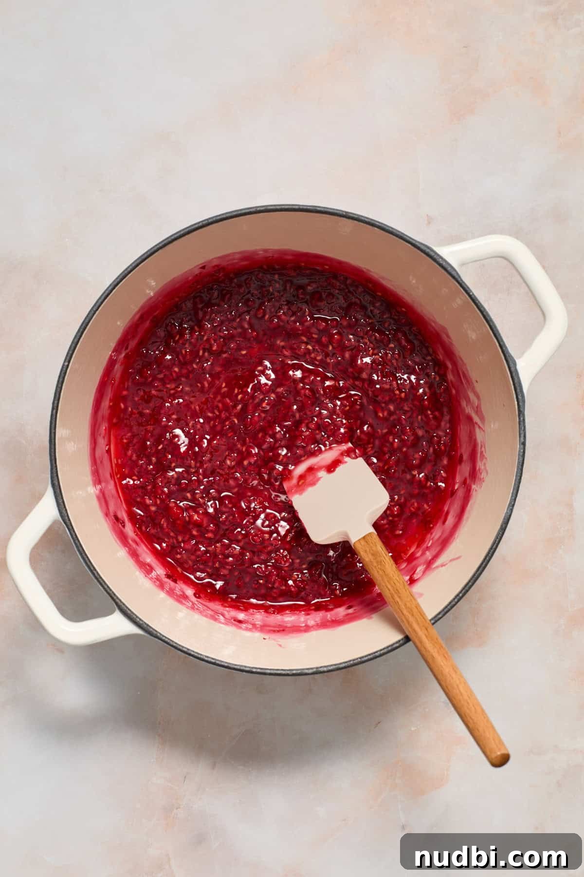 White Chocolate Raspberry Cheesecake Bars Recipe 5 Raspberries cooking in pot with spatula.