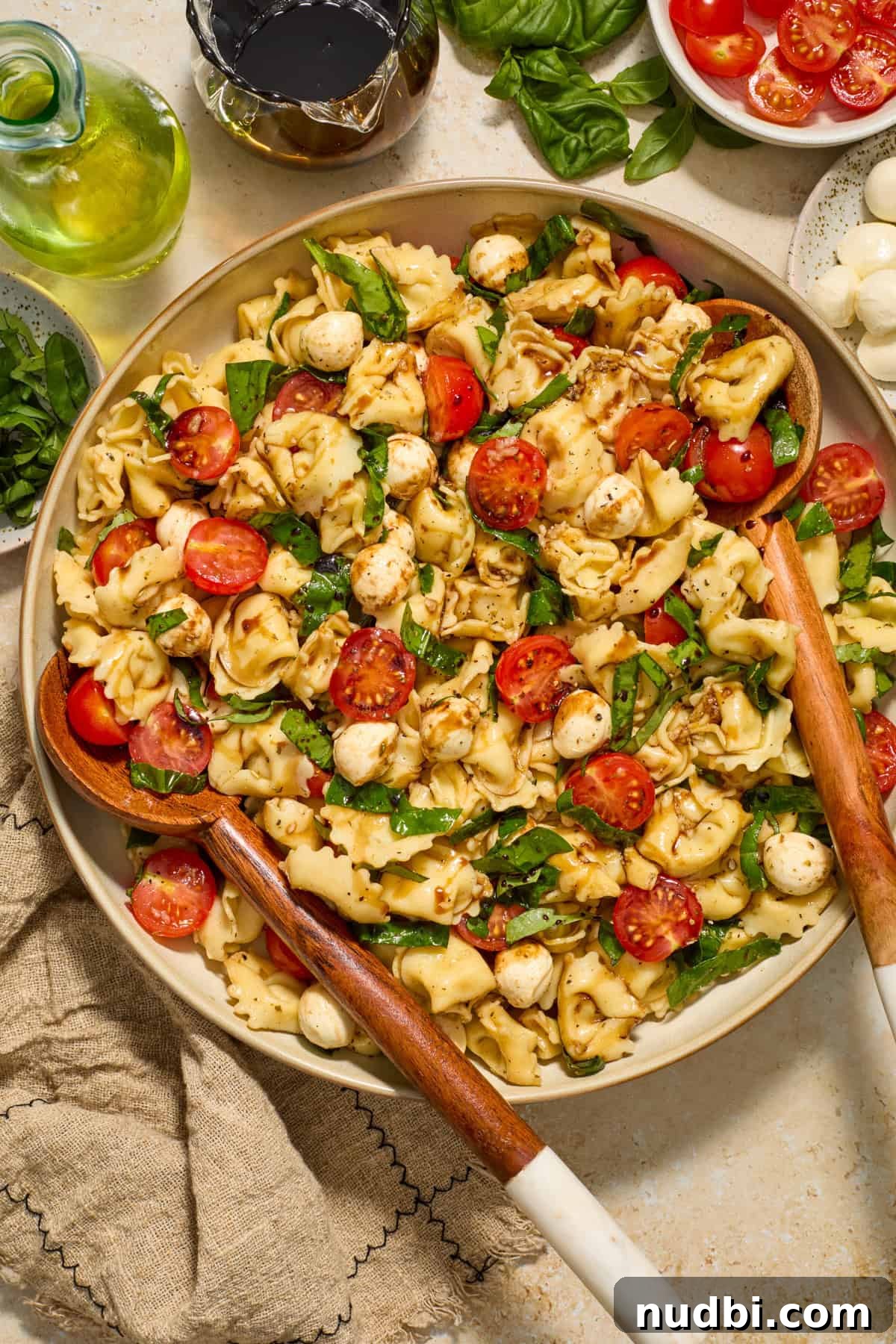 Caprese Tortellini Salad with Cherry Tomatoes and Basil 2 Serving dish with tortellini caprese pasta salad with salad utensils.