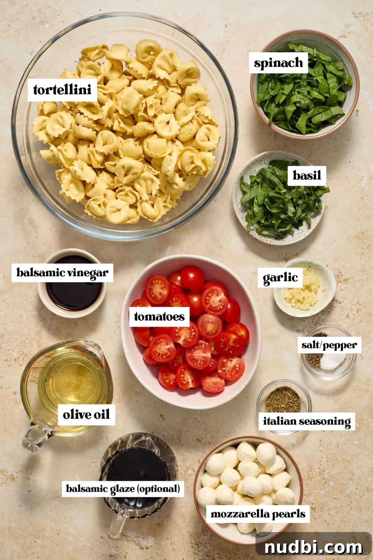 Caprese Tortellini Salad with Cherry Tomatoes and Basil 4 Tomatoes, mozzarella, tortellini, olive oil and other labeled ingredients on counter.