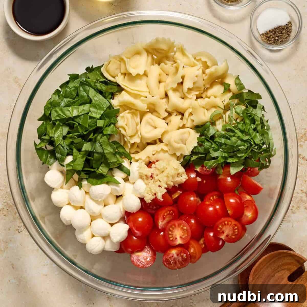 Caprese Tortellini Salad with Cherry Tomatoes and Basil 6 Tomatoes, mozzarella, spinach and other ingredients added to pasta in mixing bowl.