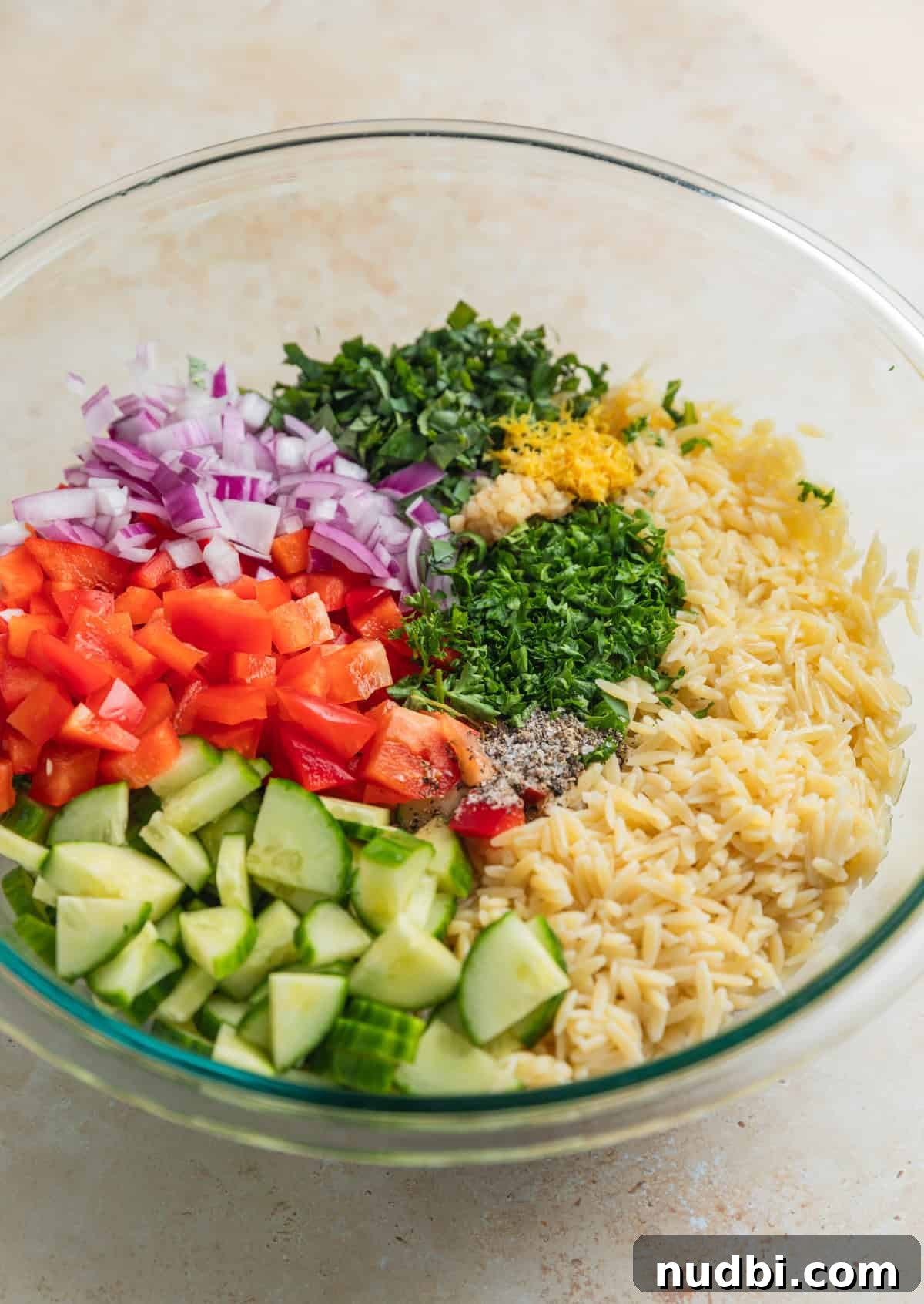 Lemon Orzo Salad with Feta, Herbs & Olive Oil Dressing 5 Orzo, lemon zest, cucumber, peppers and other ingredients in glass mixing bowl.