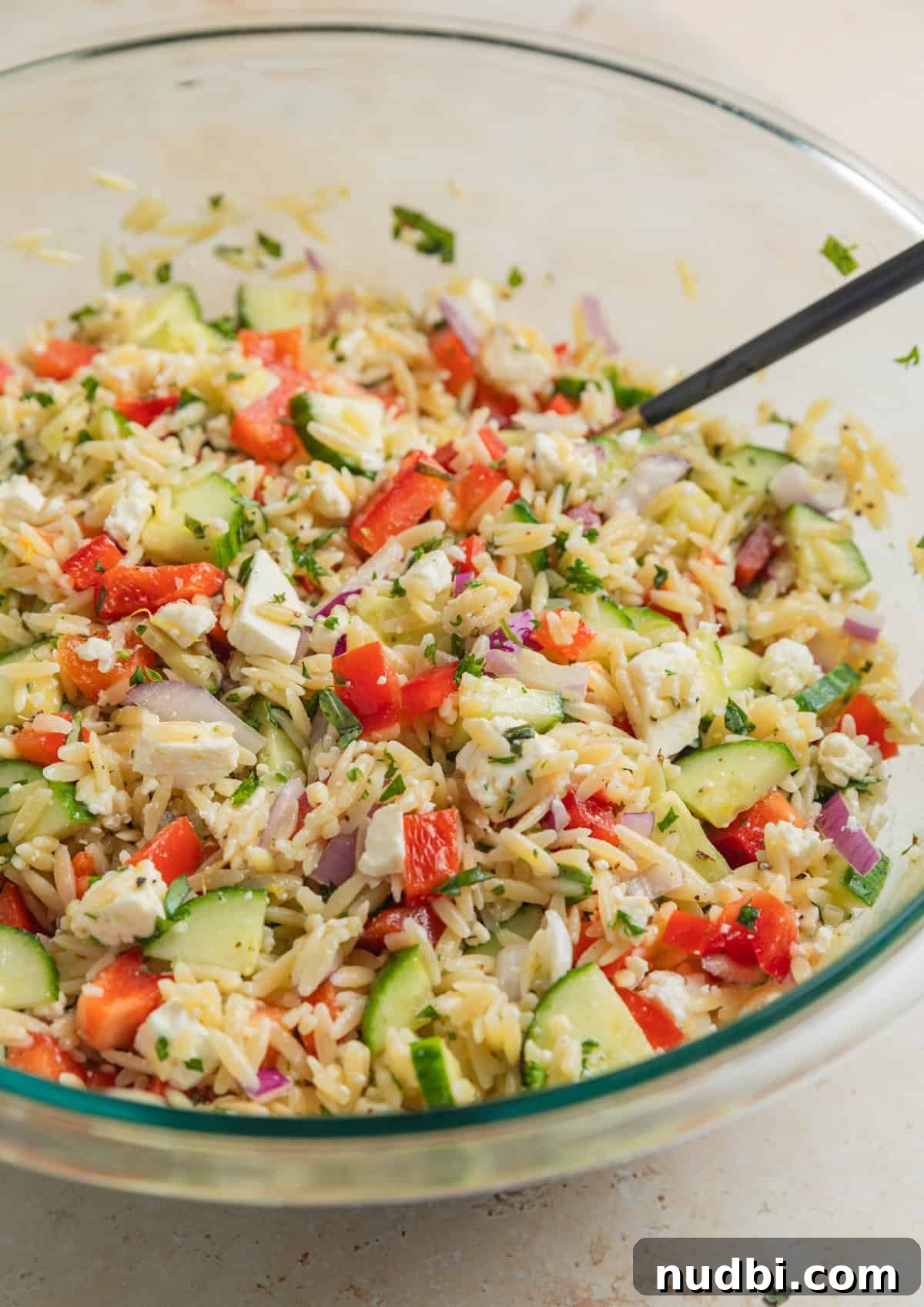 Lemon Orzo Salad with Feta, Herbs & Olive Oil Dressing 8 Prepared lemon orzo salad with spoon in glass mixing bowl.