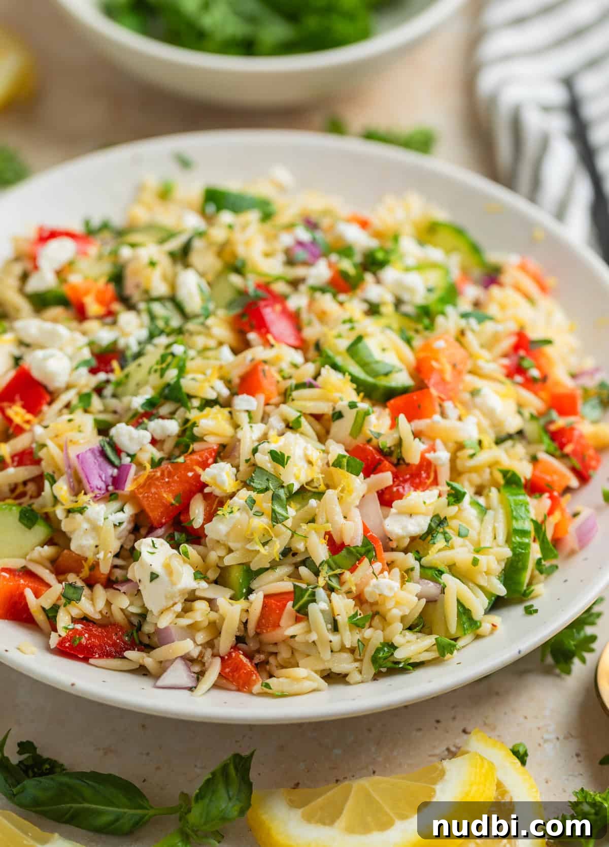 Lemon Orzo Salad with Feta, Herbs & Olive Oil Dressing 9 Orzo salad with feta, basil, parsley, cucumbers and more in white bowl.