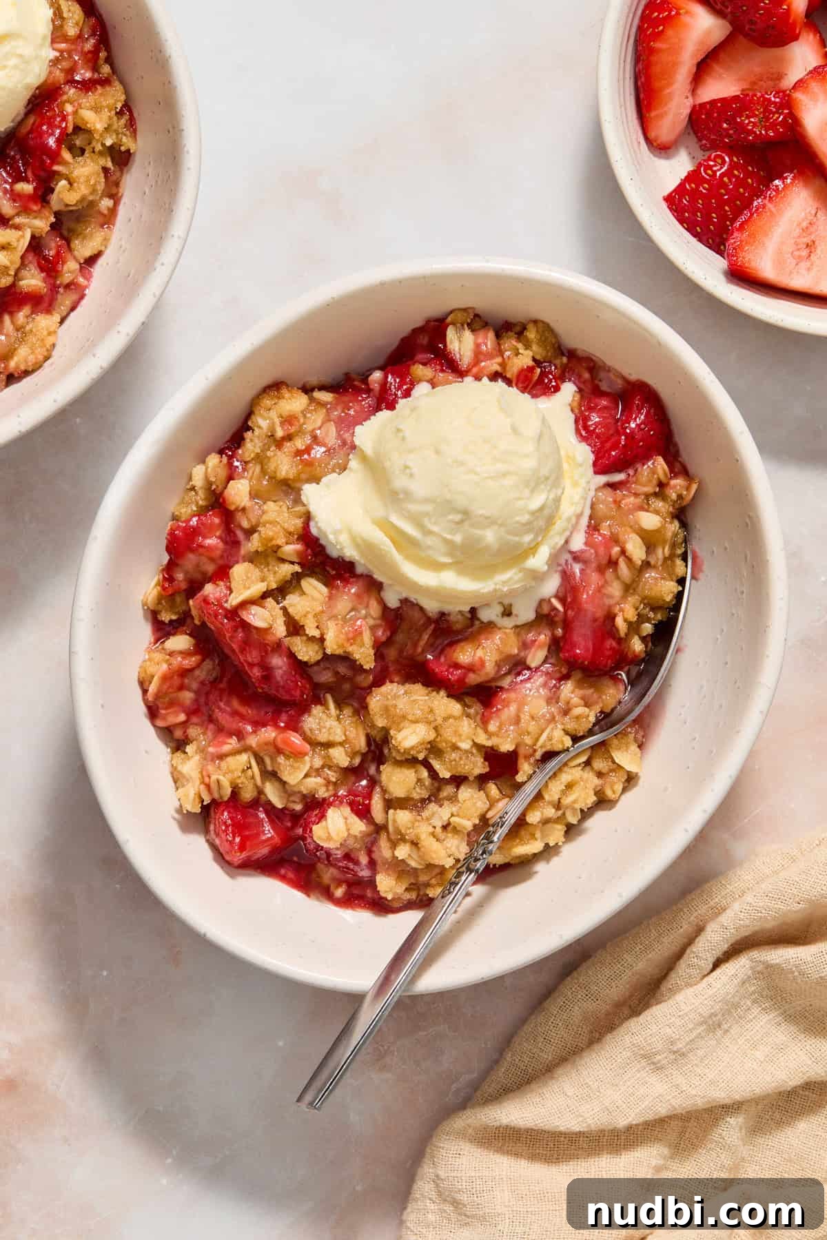Strawberry Crumble Recipe with Buttery Oat Topping 2 White dish with serving of strawberry crumble topped with vanilla ice cream.