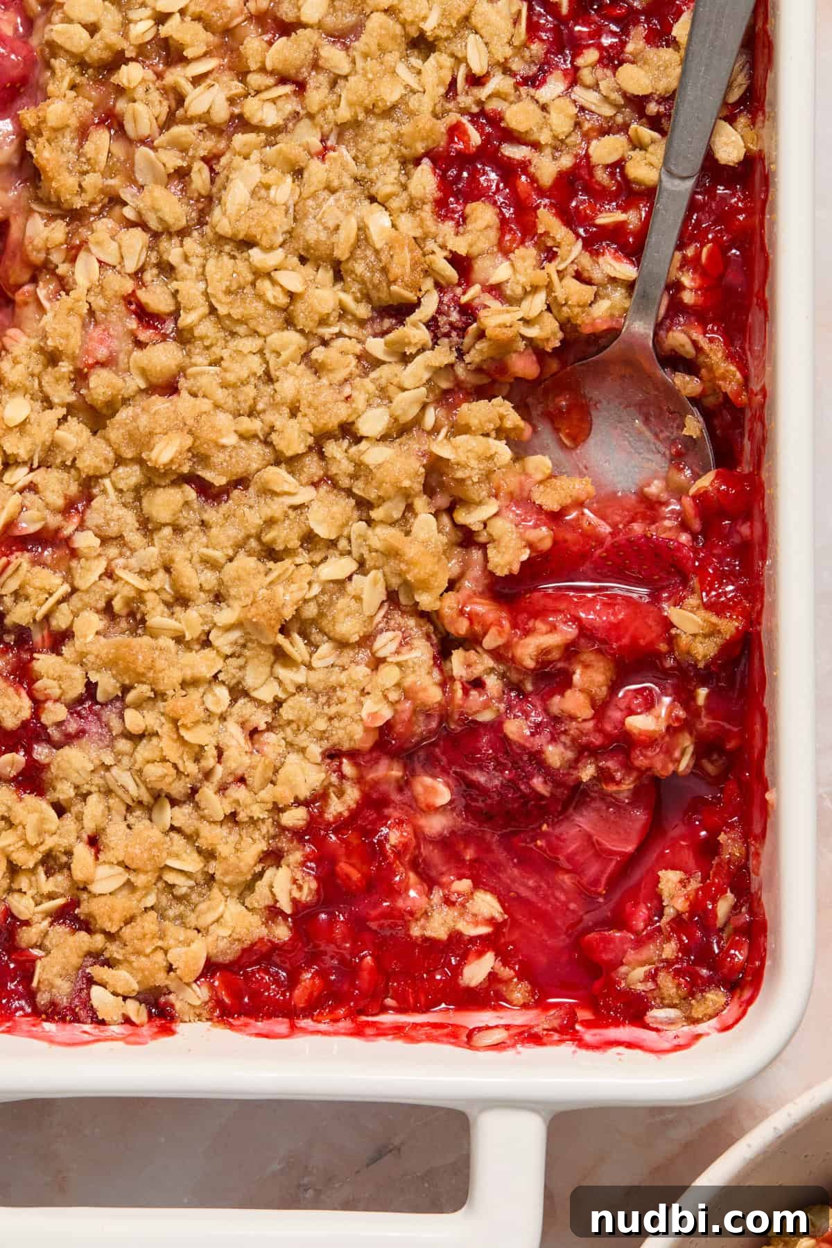 Strawberry Crumble Recipe with Buttery Oat Topping 3 Spoon scooping into strawberry crisp in baking dish.
