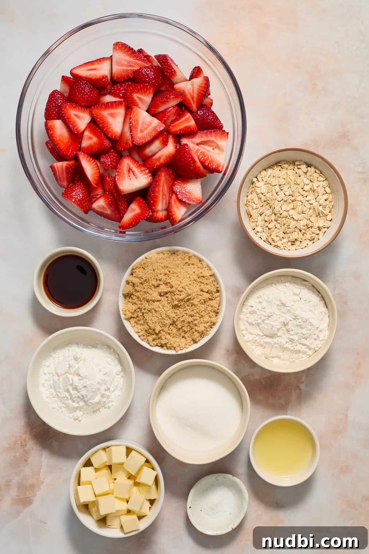Strawberry Crumble Recipe with Buttery Oat Topping 4 Oats, butter, brown sugar, vanilla and other ingredients in dishes on surface.