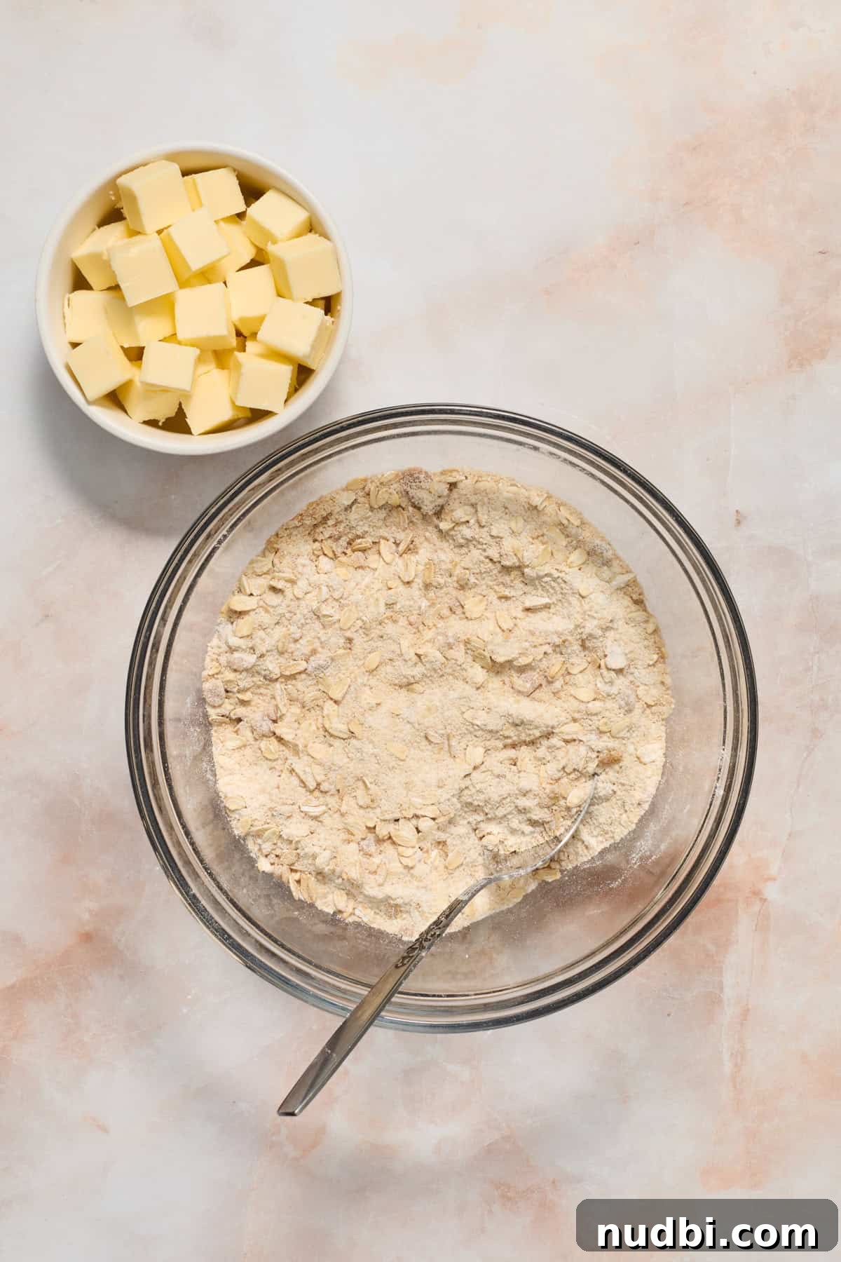 Strawberry Crumble Recipe with Buttery Oat Topping 5 Flour, oats and brown sugar mixed in glass bowl with cubed butter in bowl to the side.