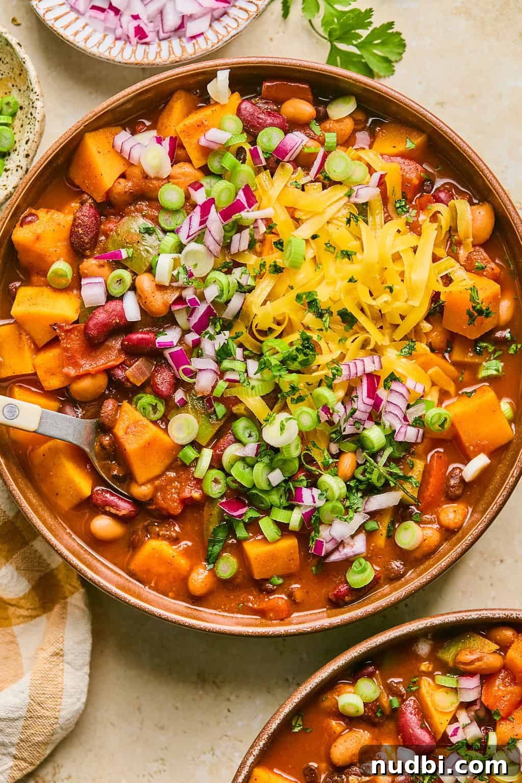 Hearty Butternut Squash Chili Recipe for Cozy Weeknights 2 Bowl of butternut squash chili with cheese, onion and cilantro garnish on top.