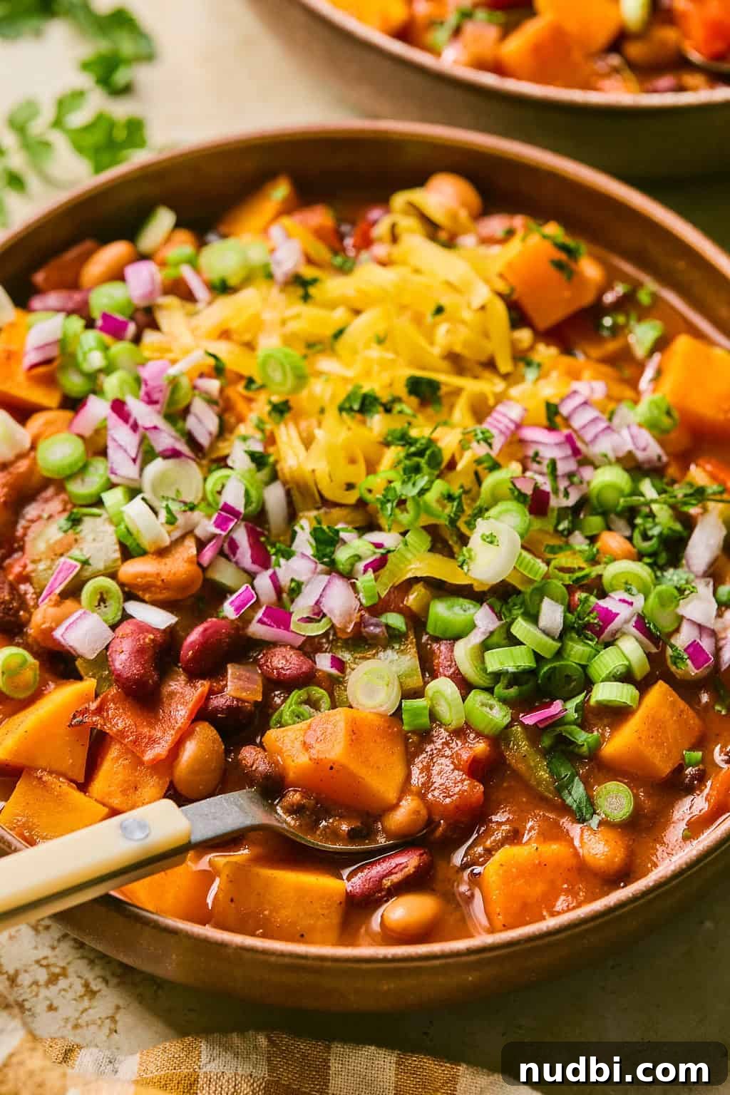 Hearty Butternut Squash Chili Recipe for Cozy Weeknights 8 Bowl with spoon scooping into butternut squash chili topped with shredded cheese and onions.