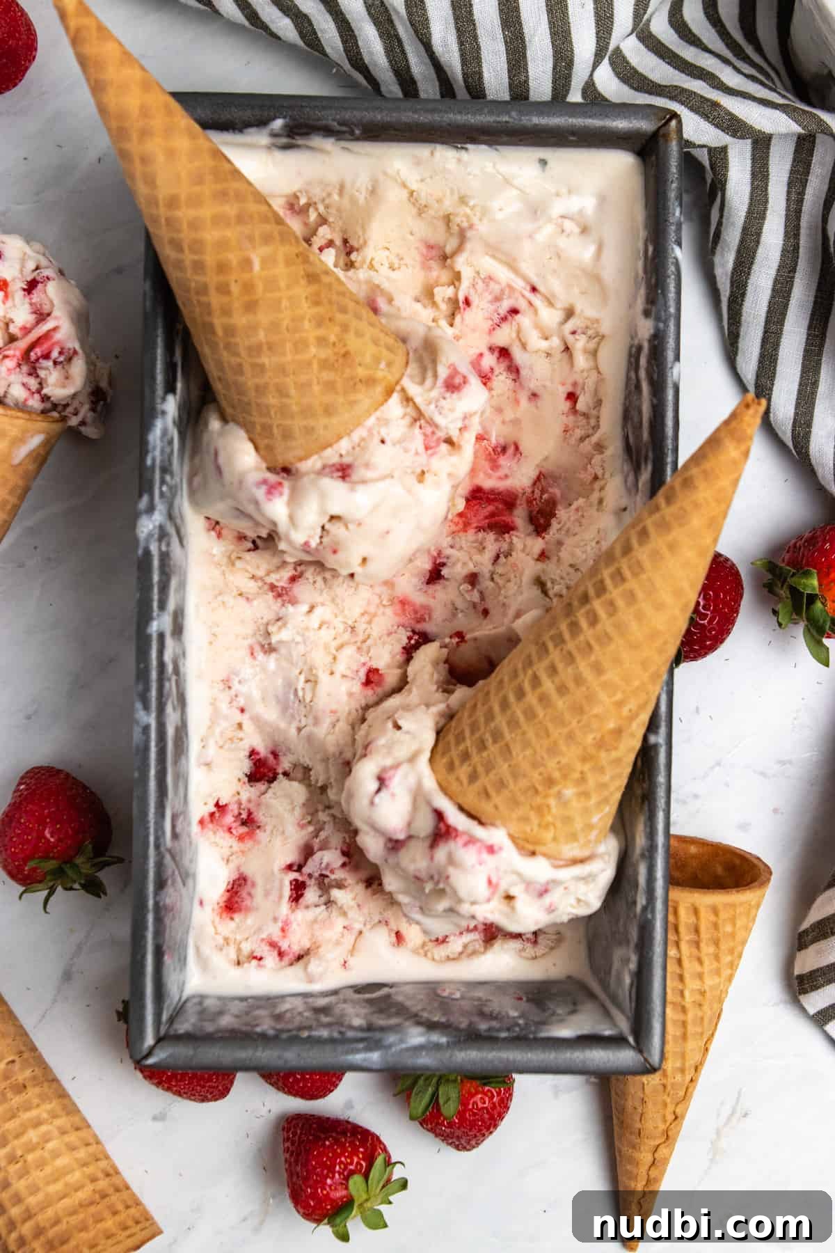 Creamy No-Churn Strawberry Ice Cream Recipe 2 Strawberry ice cream in bread pan loaf with scoops and sugar cones.