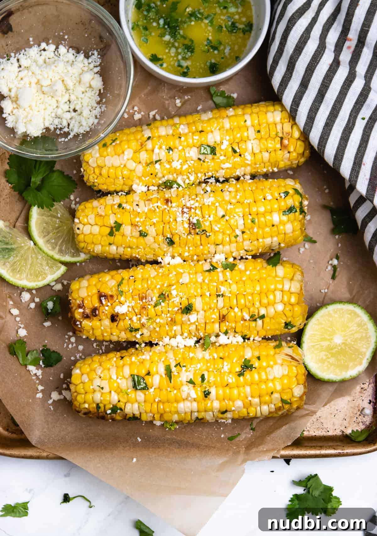 Cilantro Lime Butter Corn on the Cob (Air Fryer Recipe) 2 Overview of corn on the cob with limes and cojita cheese on parchment.