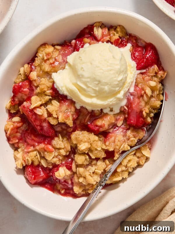 Strawberry and Peach Shortcake Recipe | Summer Dessert Guide 17 Strawberry crumble served in bowl with a scoop of ice cream and spoon scooping in.