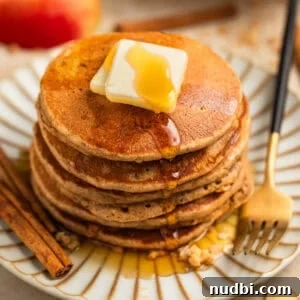 Apple Cinnamon Oatmeal Pancakes Recipe: Fluffy, Whole-Grain Breakfast 13 Stack of pancakes on plate with butter and maple syrup and cinnamon sticks beside.