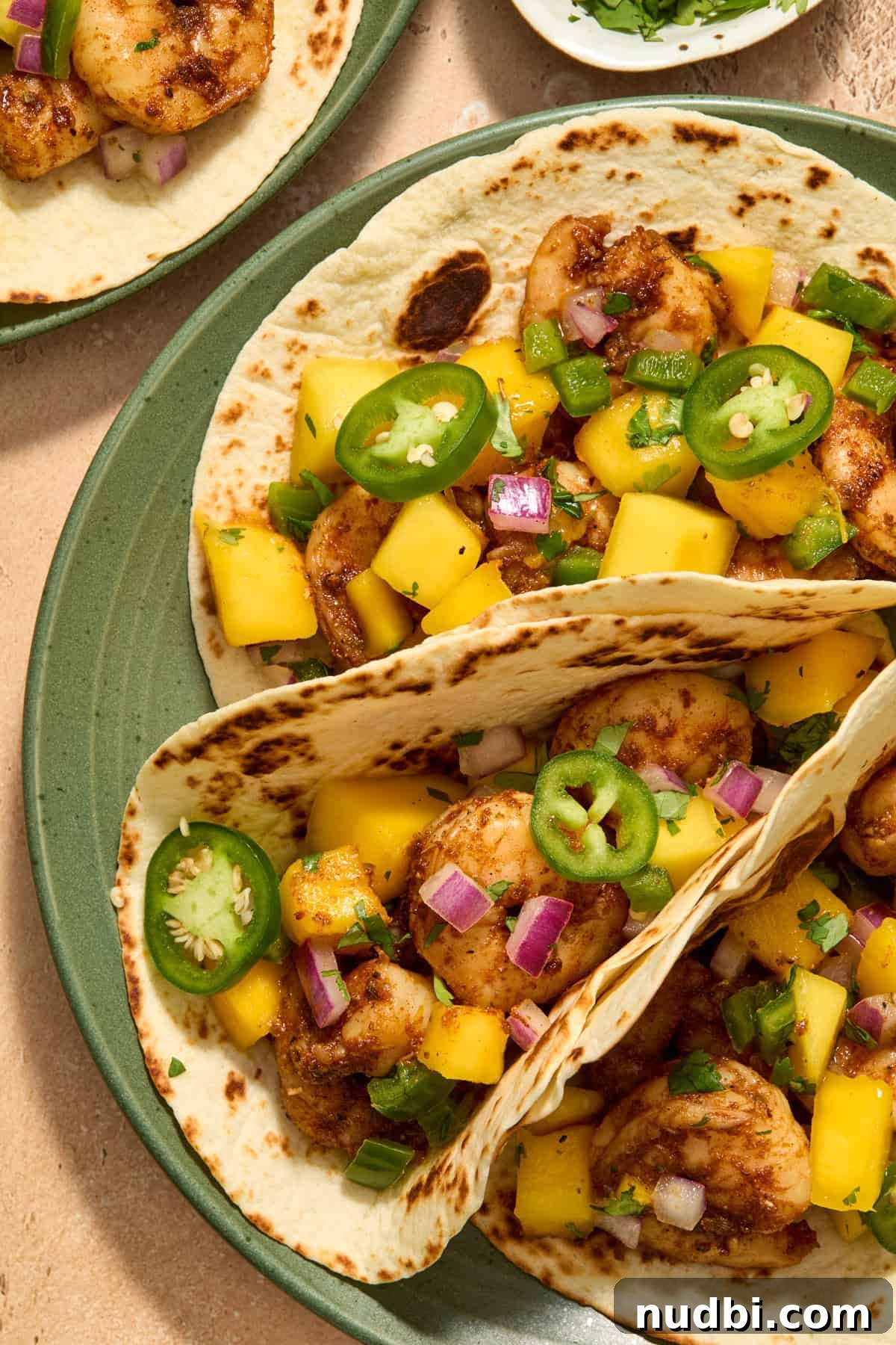 Mango Salsa Shrimp Tacos with Lime Crema 9 View of tortillas with spicy shrimp and mango salsa on top on green plate.