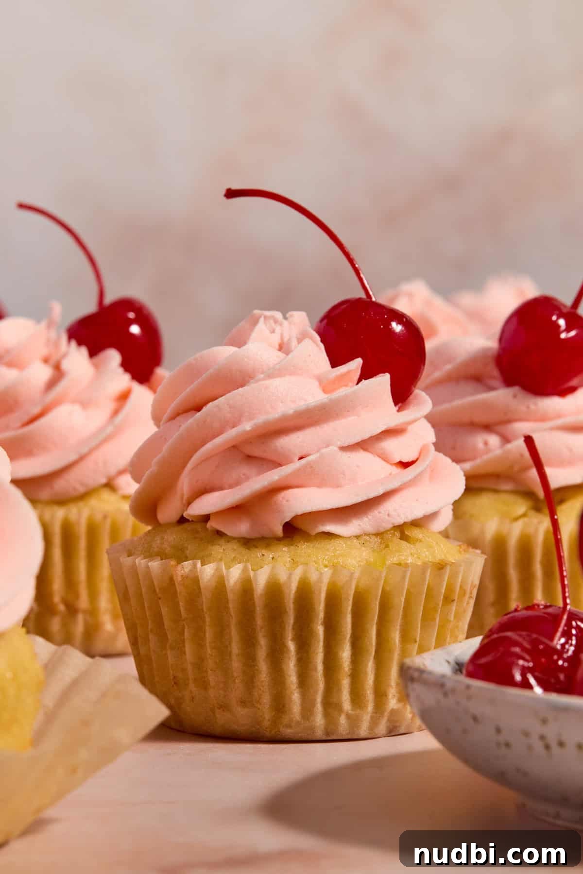 Pineapple Cupcakes with Cherry Buttercream Frosting 2 Cherry frosted pineapple cupcakes arranged on surface with maraschino cherry on top.