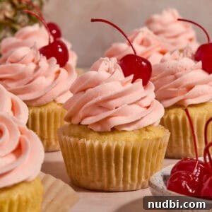 Pineapple Cupcakes with Cherry Buttercream Frosting 8 Pineapple cupcakes on surface with cherry frosting and cherry on top.