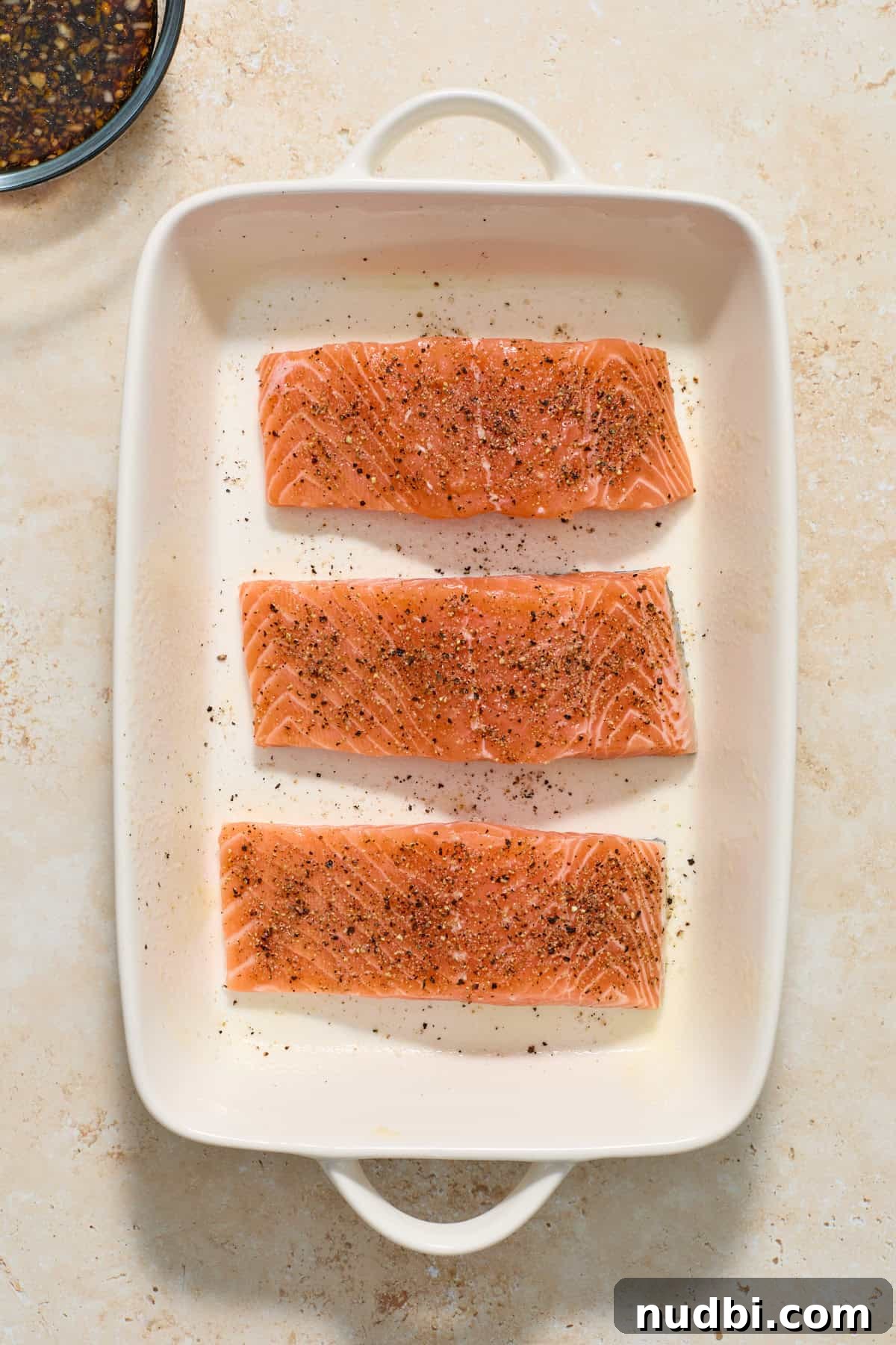 Maple Citrus Glazed Salmon with Tangy Orange Lemon Sauce 5 Salmon fillets in white baking pan seasoned with salt and pepper.