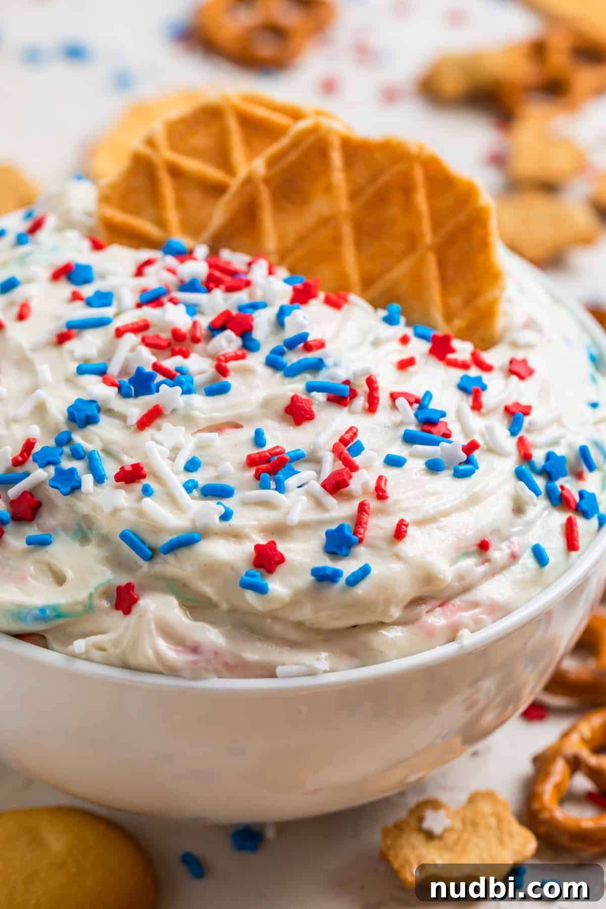 Patriotic Funfetti Dip Recipe for 4th of July Parties 2 White bowl with red, white and blue funfetti cake dip with waffle cookie pieces dipped in.