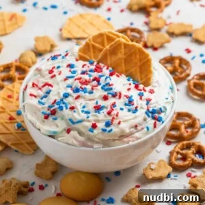 Patriotic Funfetti Dip Recipe for 4th of July Parties 14 White bowl with funfetti cake dip with two waffle cookies dipping into it.