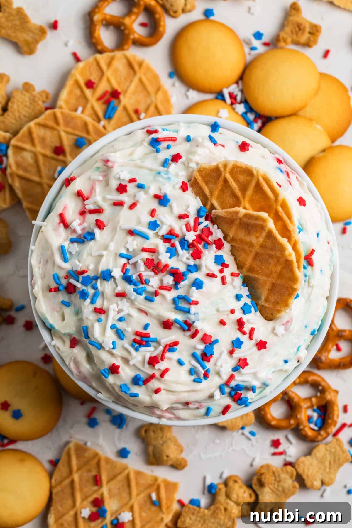 Patriotic Funfetti Dip Recipe for 4th of July Parties 3 Dunkaroo dip in white bowl with red, white and blue sprinkles on top and cookies and pretzels surrounding.