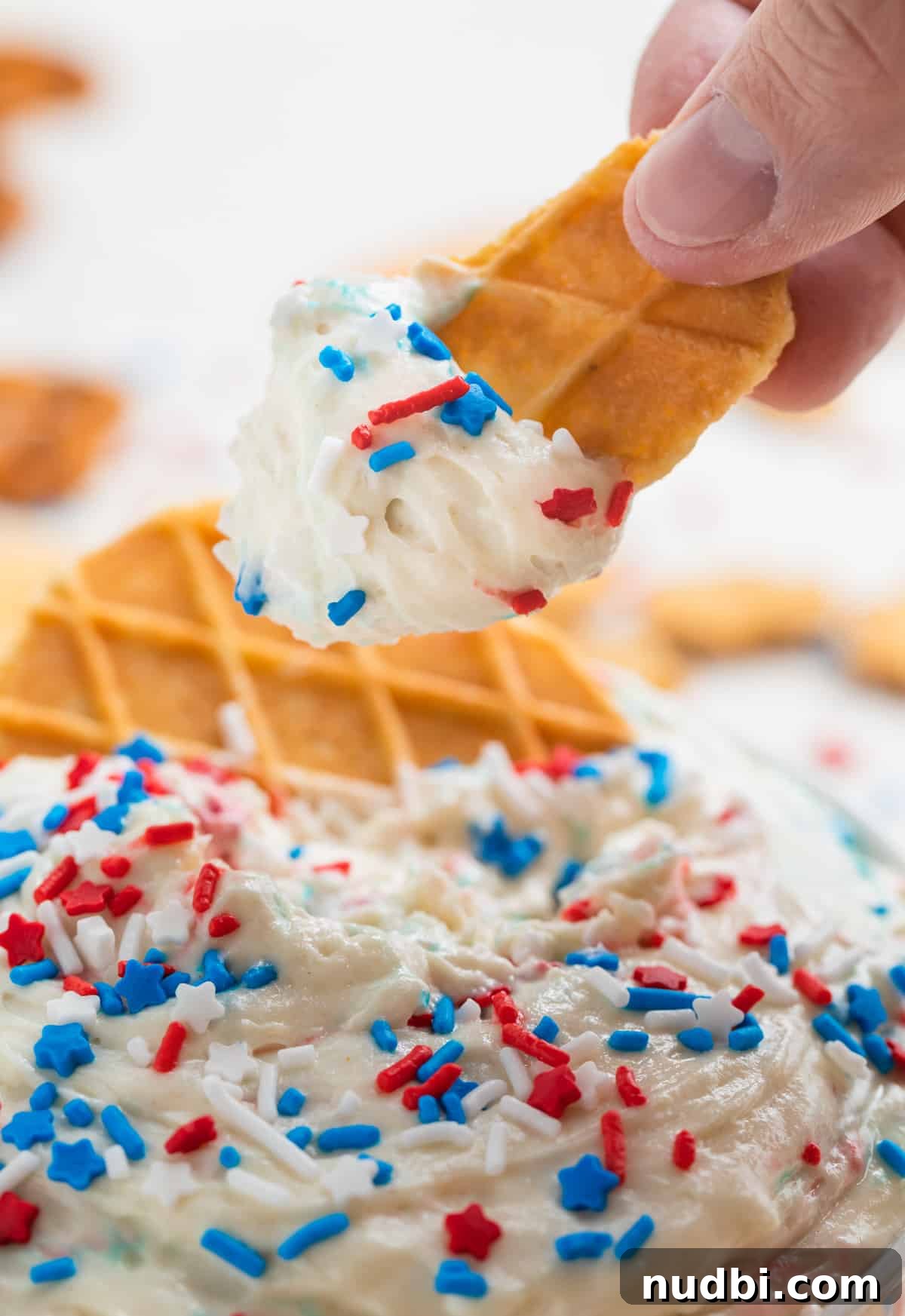 Patriotic Funfetti Dip Recipe for 4th of July Parties 8 Waffle cookie piece with patriotic funfetti dip on end topped with red, white and blue sprinkles.