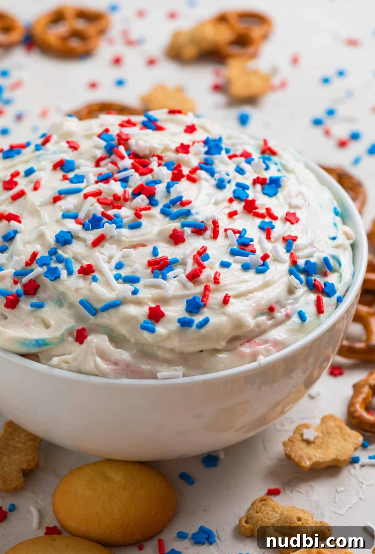 Patriotic Funfetti Dip Recipe for 4th of July Parties 9 Red, white and blue patriotic funfetti dip in white bowl with sprinkles on top and cookies surrounding.
