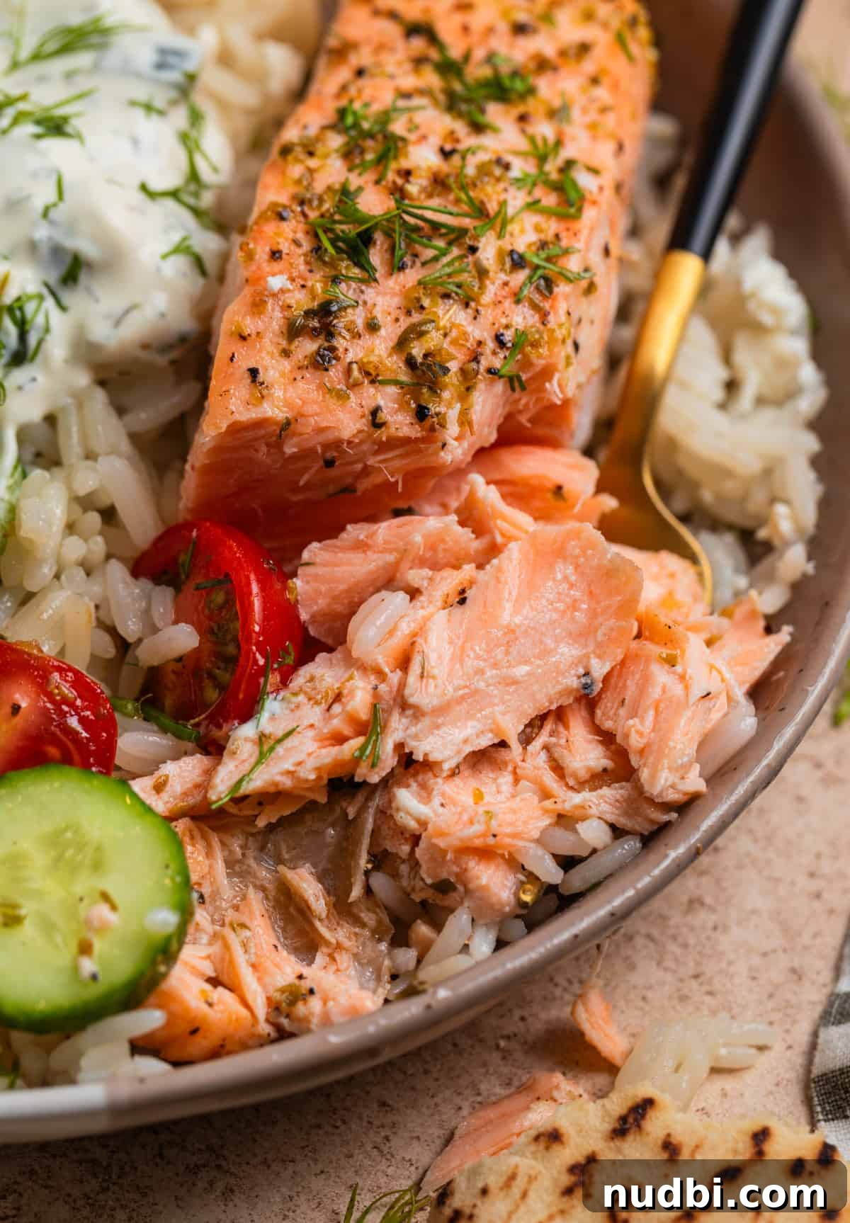 Greek Salmon Rice Bowls with Tzatziki & Lemon Dill Rice 9 Salmon in dish with rice and veggies with fork and part of the salmon flaked.