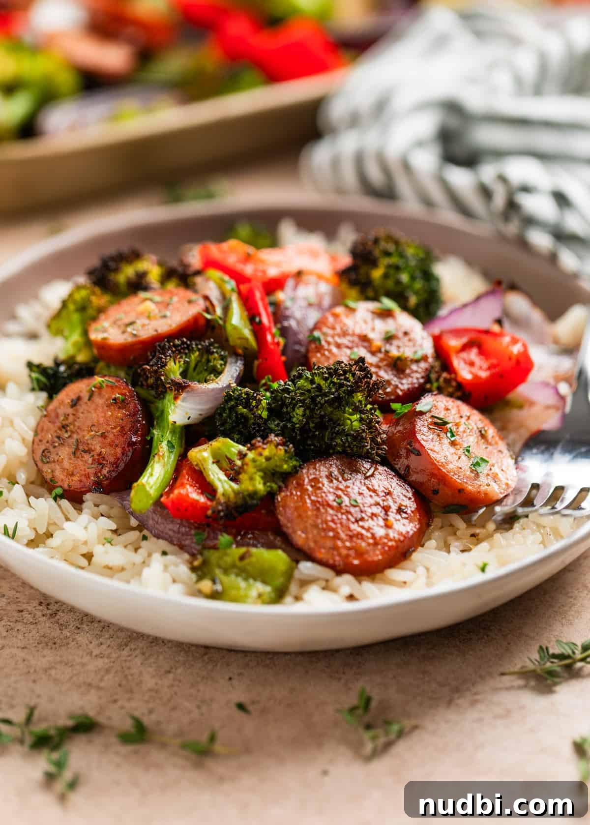 One-Pan Sausage and Veggie Sheet Pan Dinner 3 Kielbasa pork sausage and veggies over rice on plate with fork.