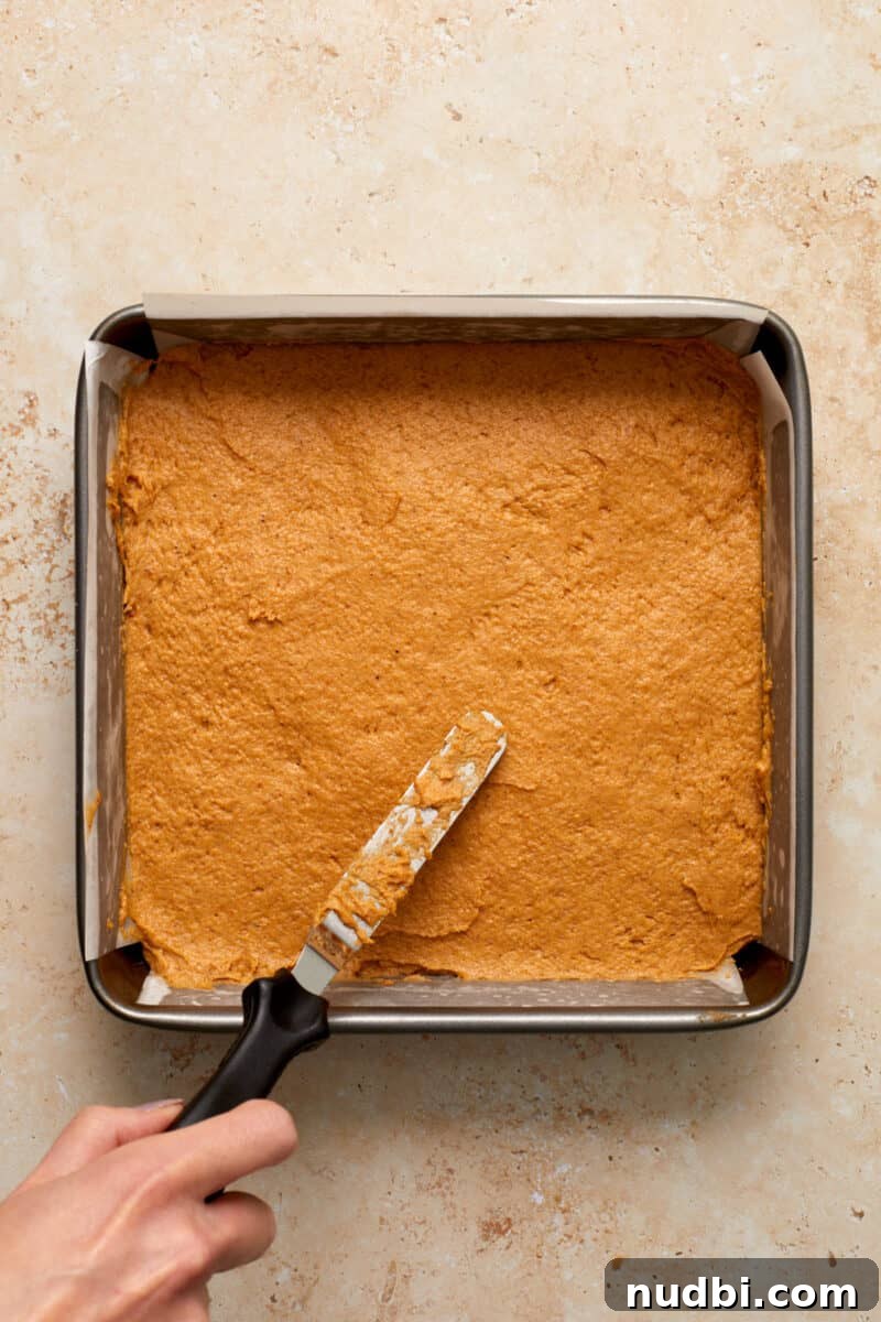 Cinnamon Streusel Pumpkin Coffee Cake Recipe for Fall Baking 12 Pumpkin coffee cake in parchment lined baking pan with spatula spreading over top.