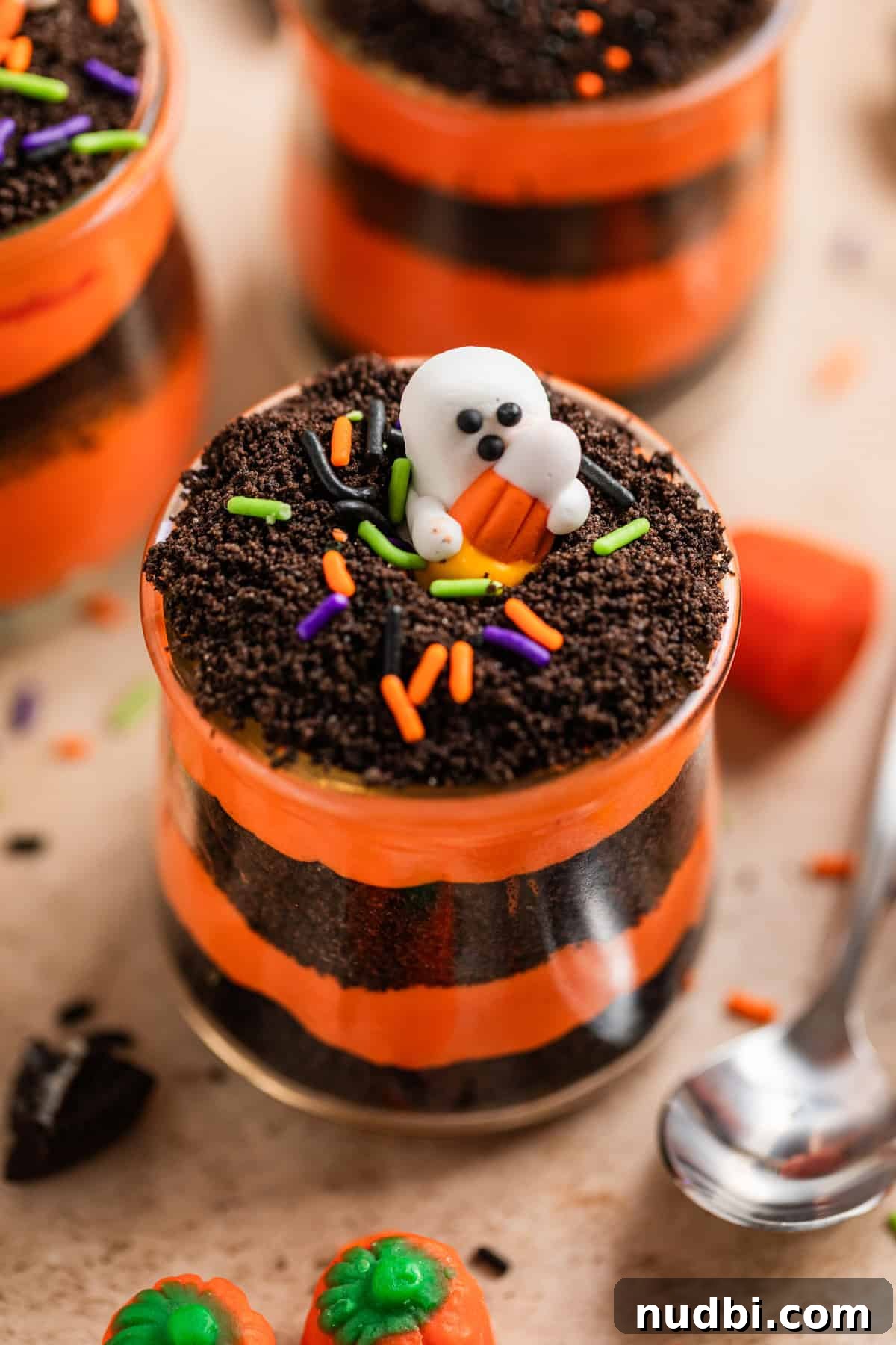 Halloween Oreo Dirt Cake Recipe for Spooky No-Bake Dessert 2 Halloween dirt cake layered in small glass cup to show orange and black layers topped with sprinkles and ghost candy.