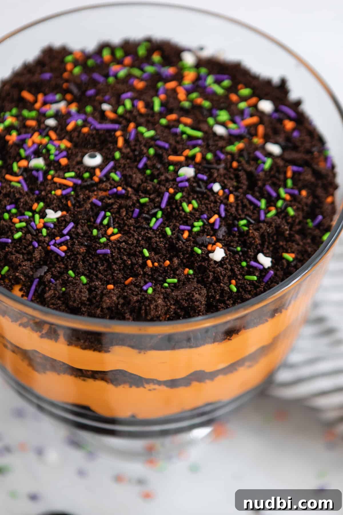Halloween Oreo Dirt Cake Recipe for Spooky No-Bake Dessert 7 Trifle bowl with layered orange pudding and crushed Halloween Oreos.