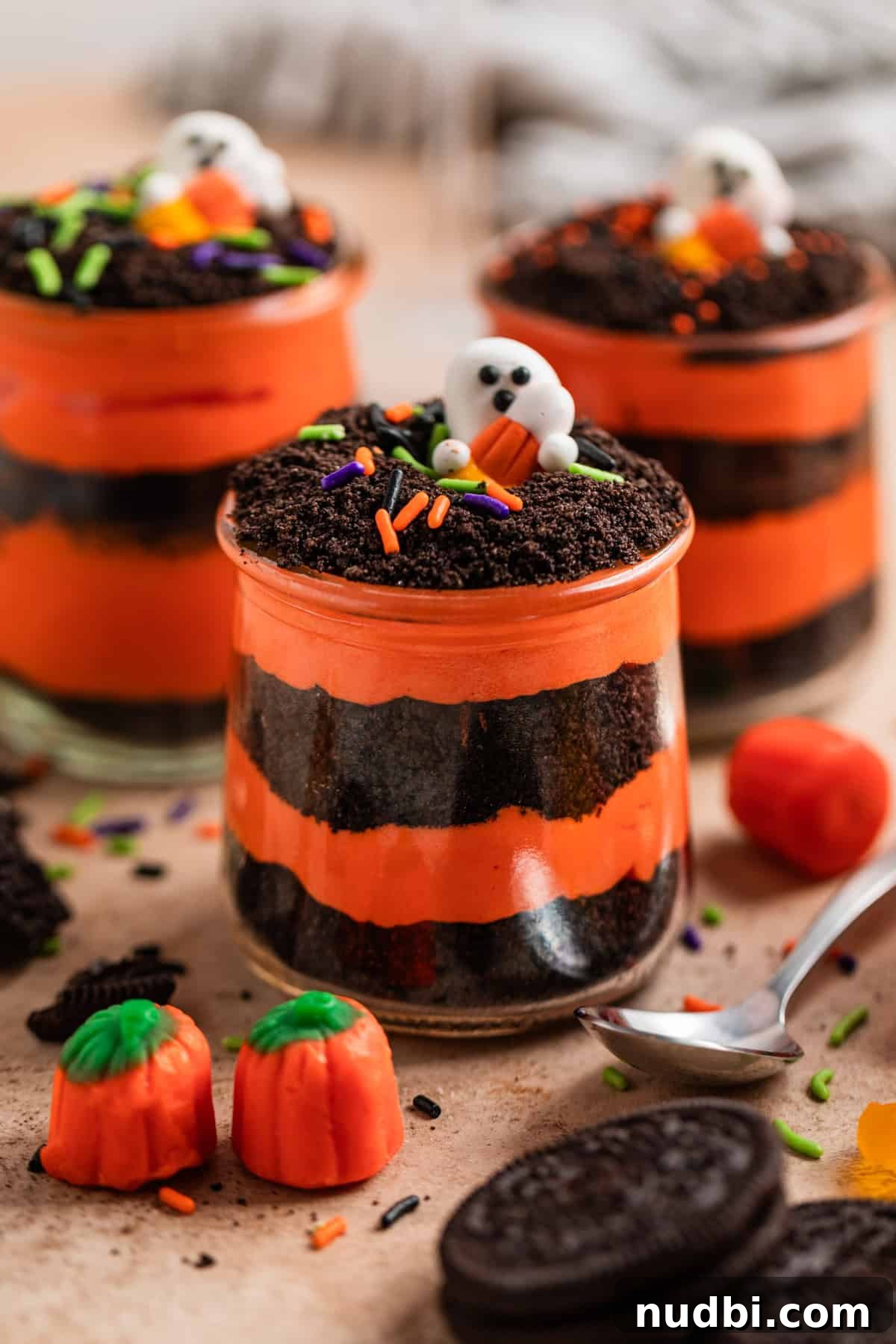Halloween Oreo Dirt Cake Recipe for Spooky No-Bake Dessert 8 Orange and black layered pudding and crushed Oreos in glass jars with Halloween themed sprinkles and candy.