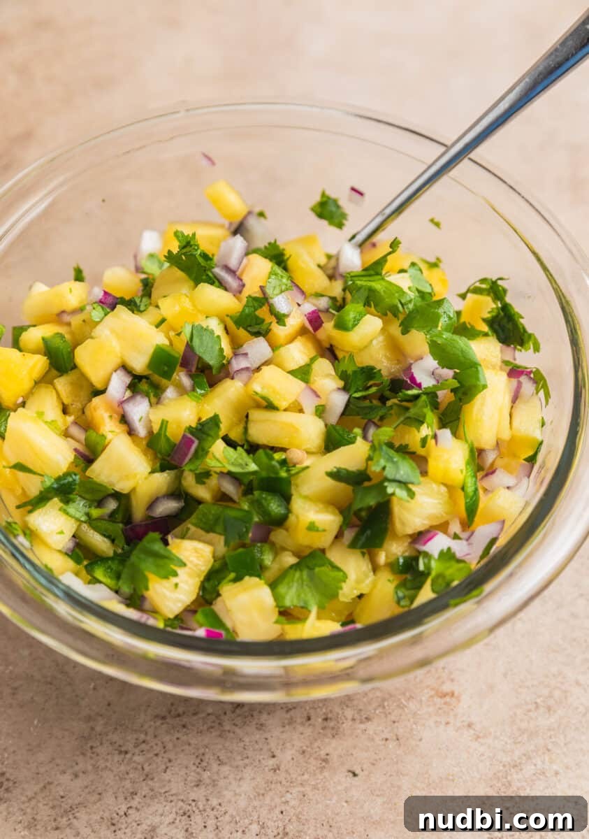 Pineapple Salsa Ground Pork Tacos: Sweet & Spicy Street-Style Recipe 6 Spoon scooping into glass bowl with pineapple salsa.