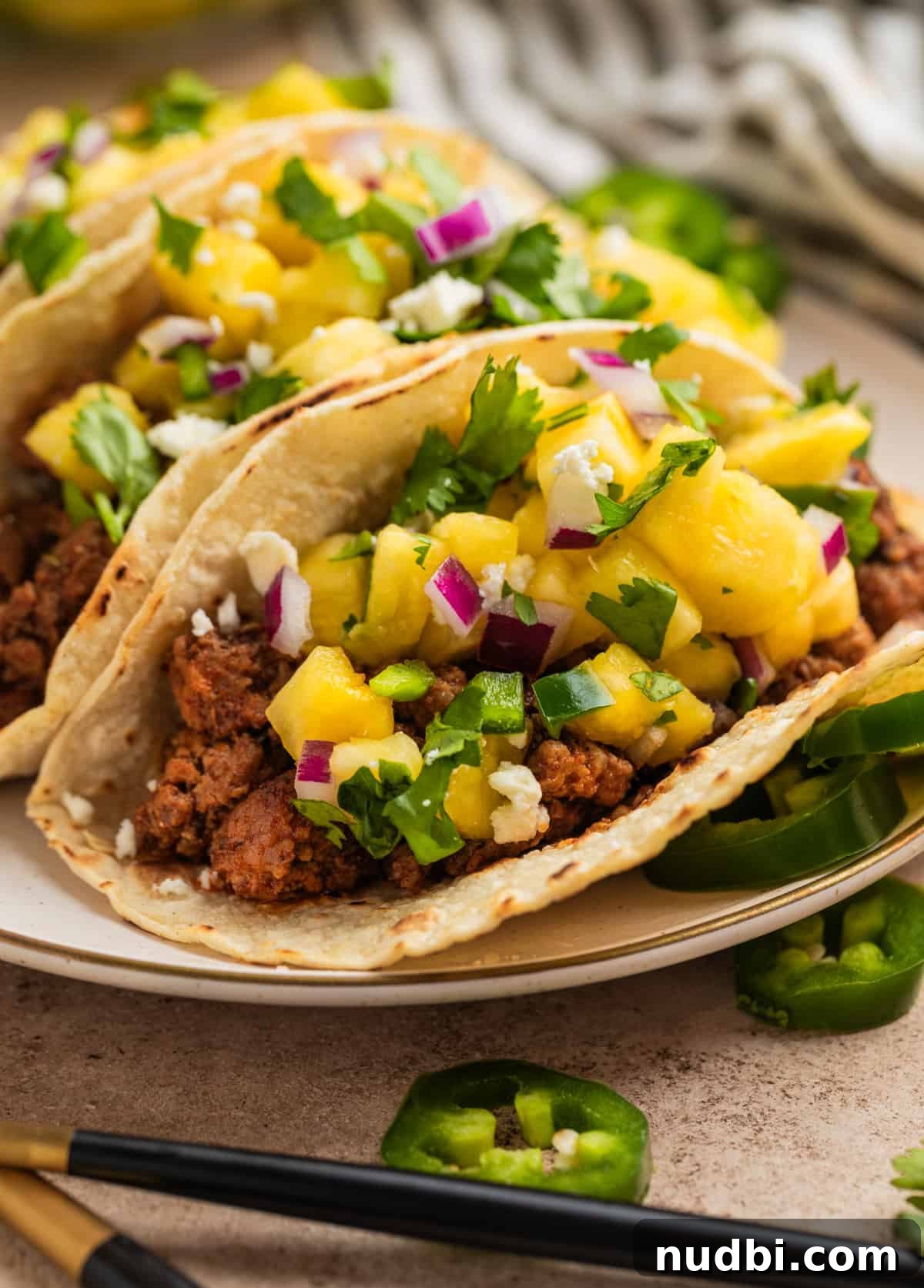 Pineapple Salsa Ground Pork Tacos: Sweet & Spicy Street-Style Recipe 9 Pork tacos topped with pineapple salsa on plate with sliced jalapeños nearby.