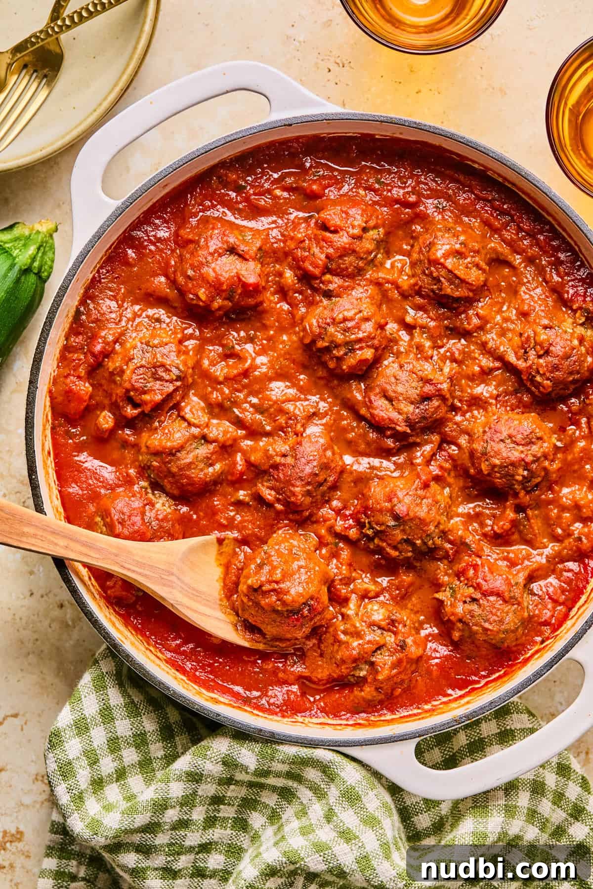 Zucchini and Beef Meatballs with Herb Sauce 5 Beef and zucchini meatballs in pot with marinara and wooden spoon.