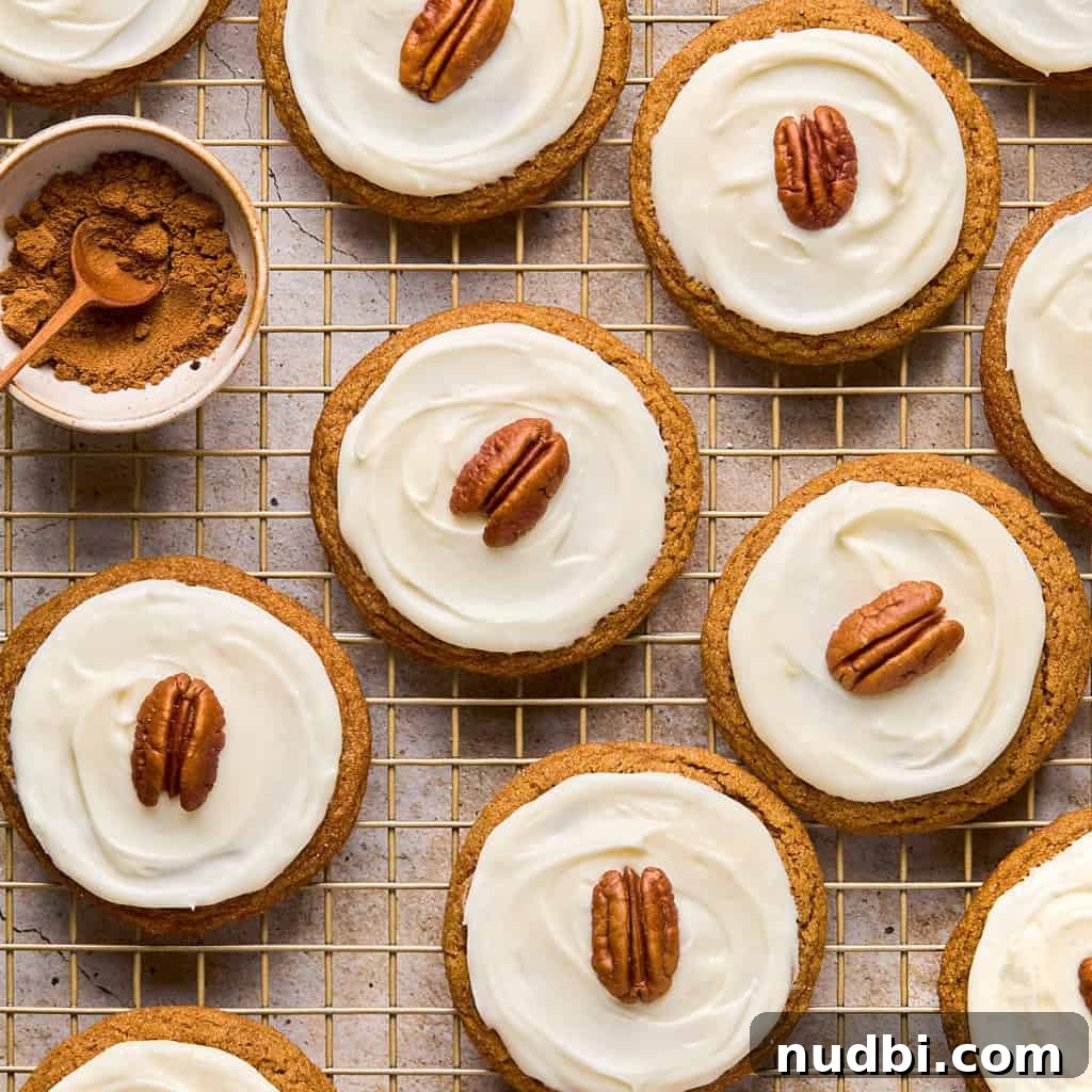Iced molasses cookies with pecan half on top arranged on cooling rack.