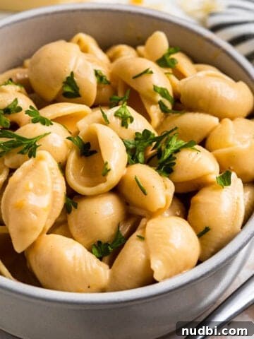 Creamy macaroni and cheese shells in clay bowl with chopped fresh parsley on top.