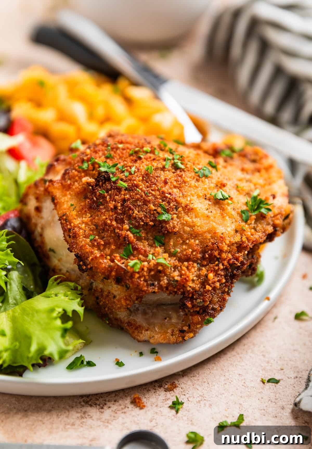 Crispy Parmesan-Crusted Air Fryer Chicken Thighs 2 Breaded parmesan air fryer chicken thigh on white plate topped with chopped parsley with macaroni and cheese and salad.
