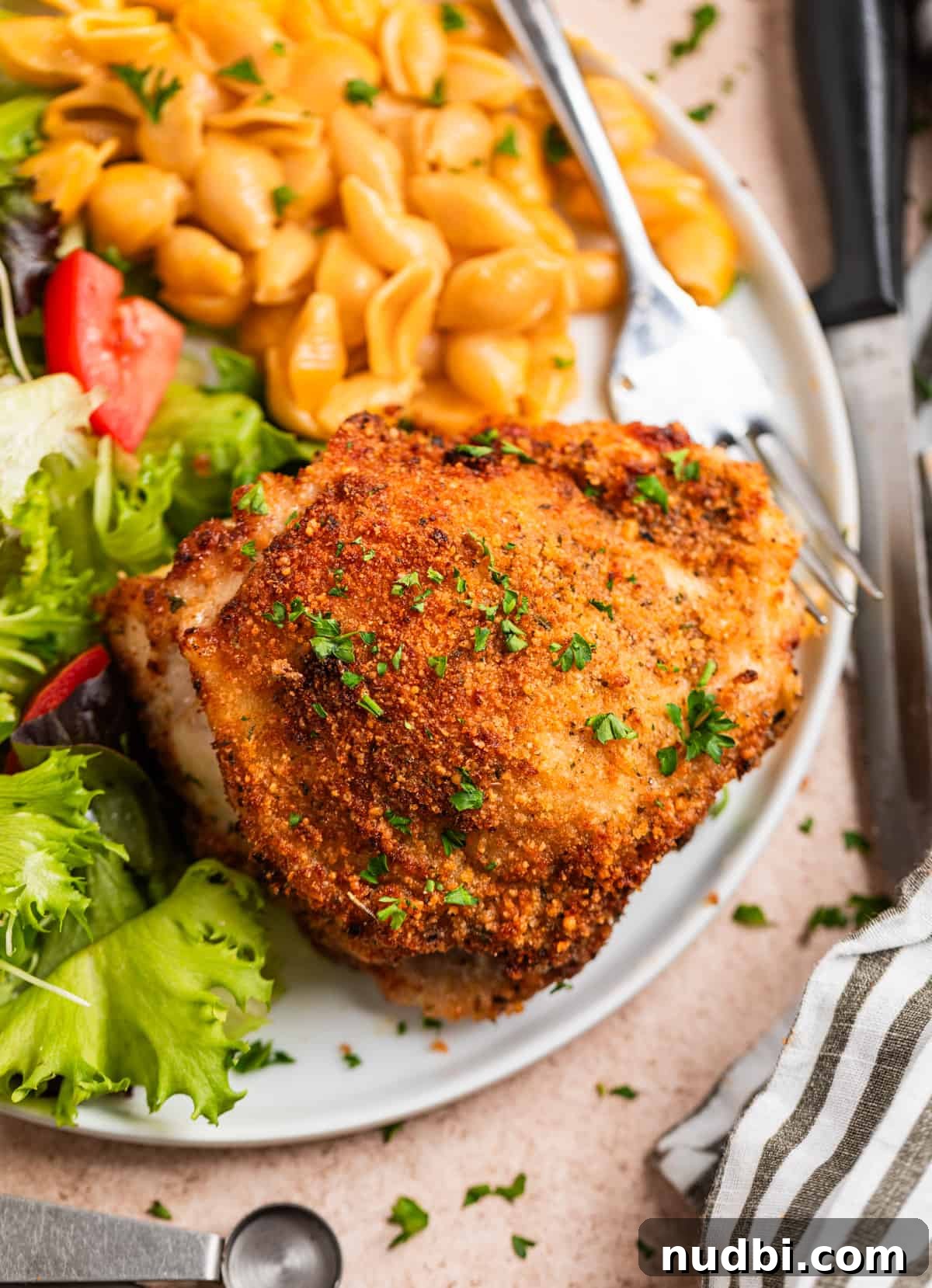Crispy Parmesan-Crusted Air Fryer Chicken Thighs 8 Overhead view of crispy parmesan chicken thigh on white plate with fork along side macaroni and a salad.