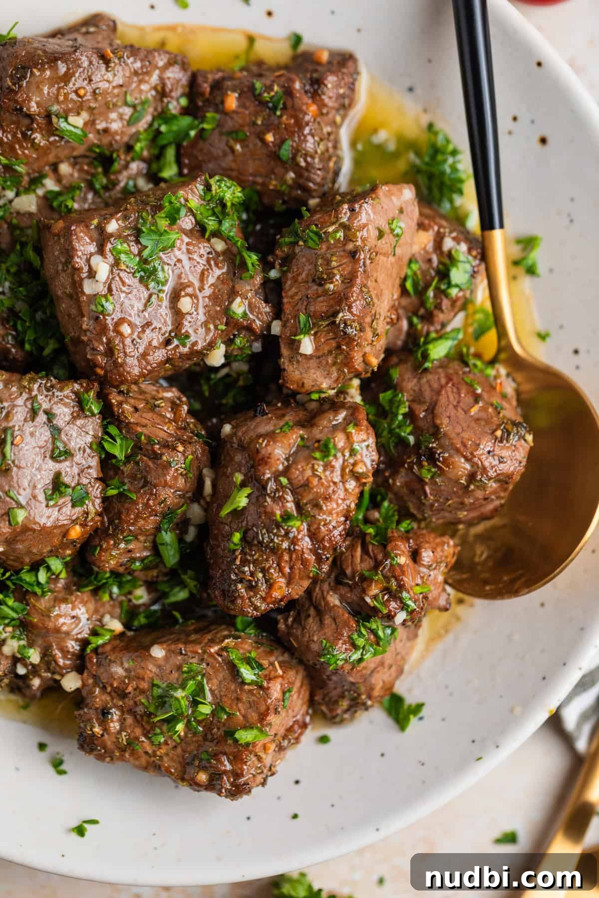 Crispy Air Fryer Steak Bites with Garlic Butter Dip 12 Overhead view of white dish with air fryer steak bites in lemon garlic butter sauce with fresh parsley over top.